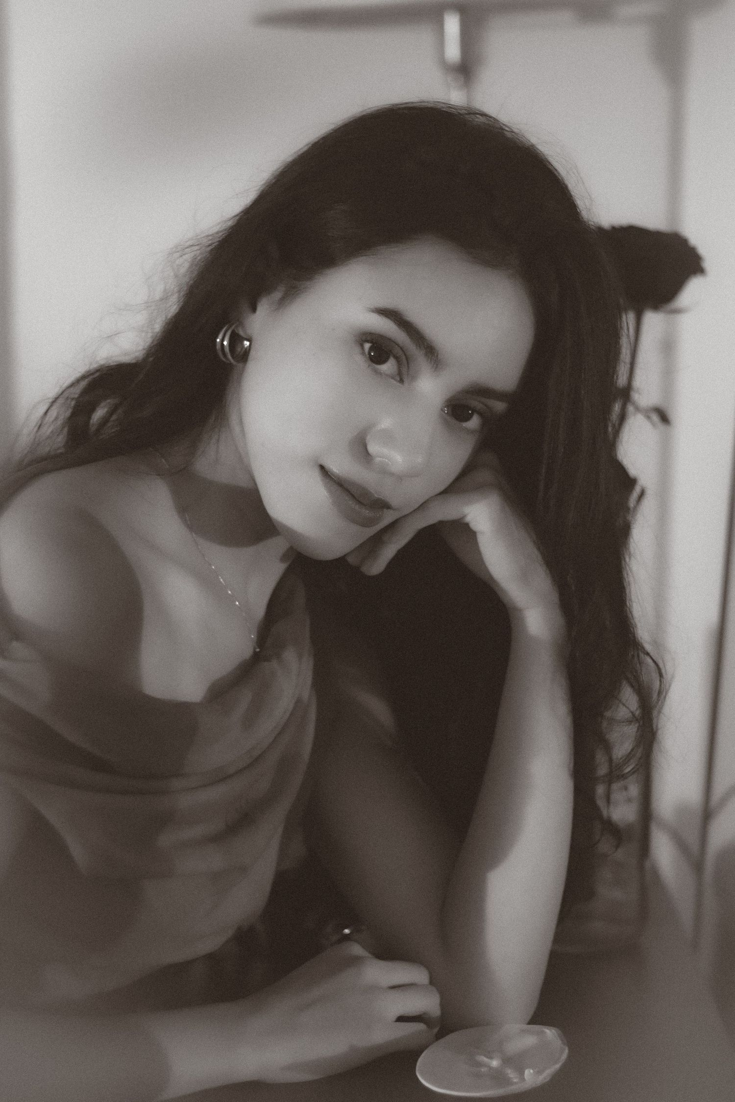 Black and white portrait of a young woman with long dark hair resting her chin on her hand, smiling softly.