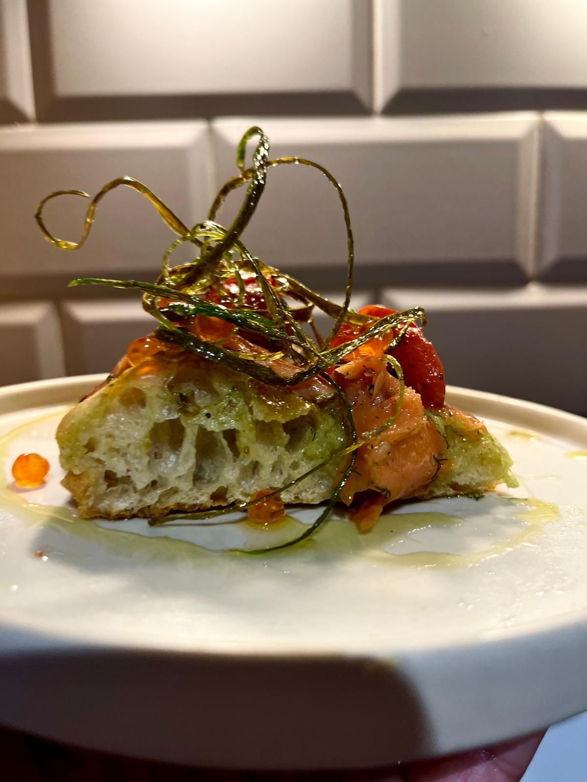 An elegant open-faced sandwich with salmon, tomatoes, avocado, and crispy garnish on artisan bread.