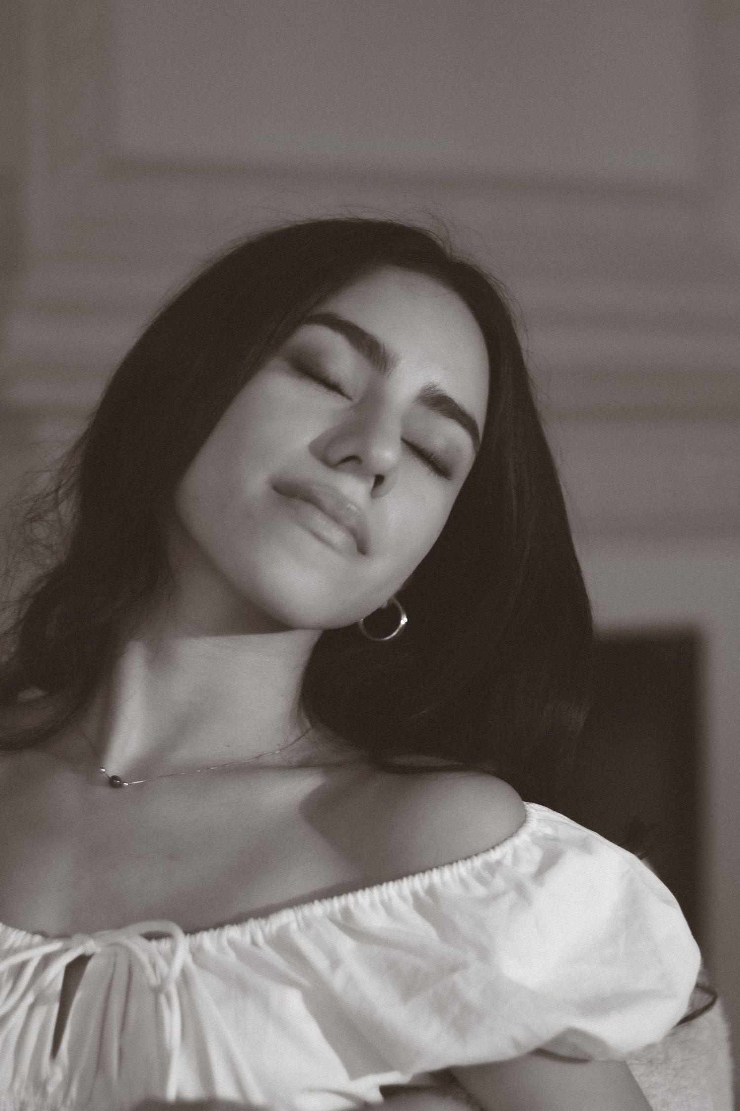 Beautiful young woman with closed eyes and hoop earring in white off-shoulder top, black and white portrait.