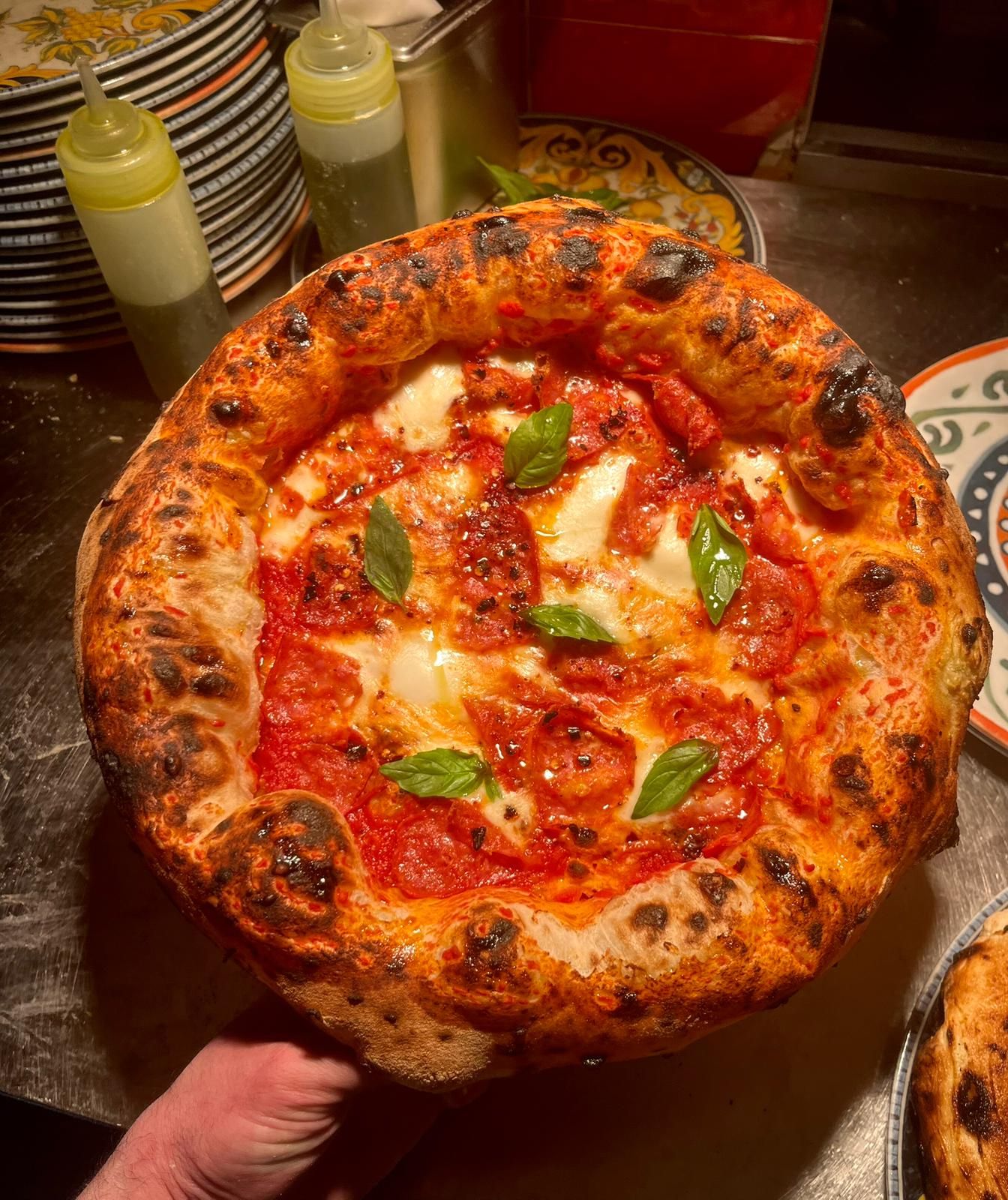 Authentic Neapolitan margherita pizza with charred crust, fresh basil, melted mozzarella, and tomato sauce on a wooden peel.
