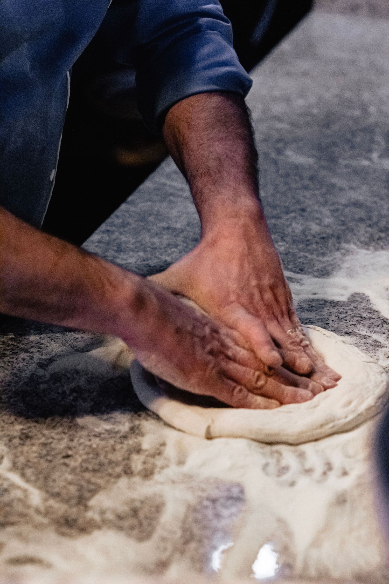 Pizzaiolo hands pressing and stretching fresh pizza dough on a flour-dusted surface.