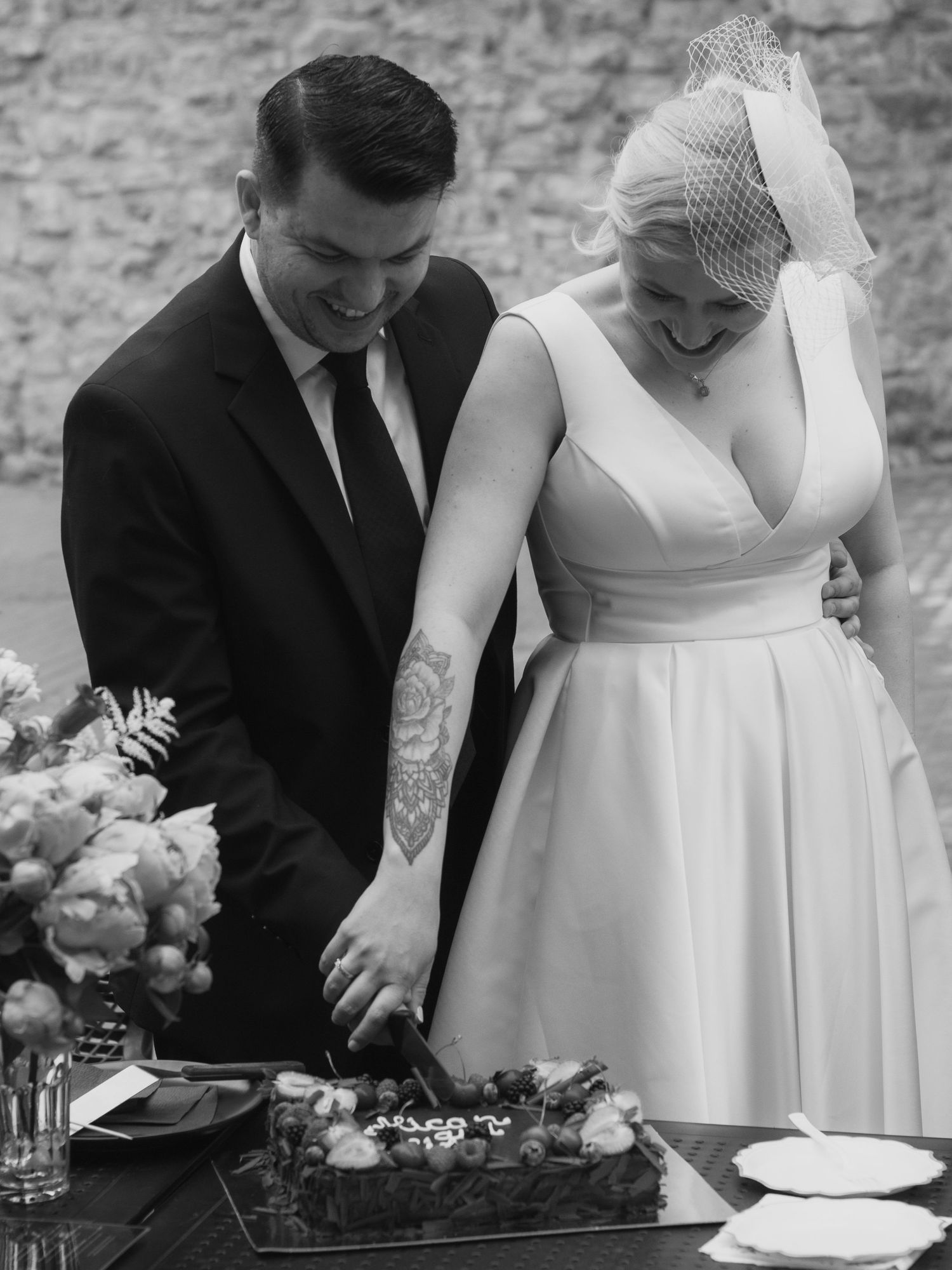 Bride and groom cutting their wedding cake together, bride wearing a birdcage veil and groom in a black suit.