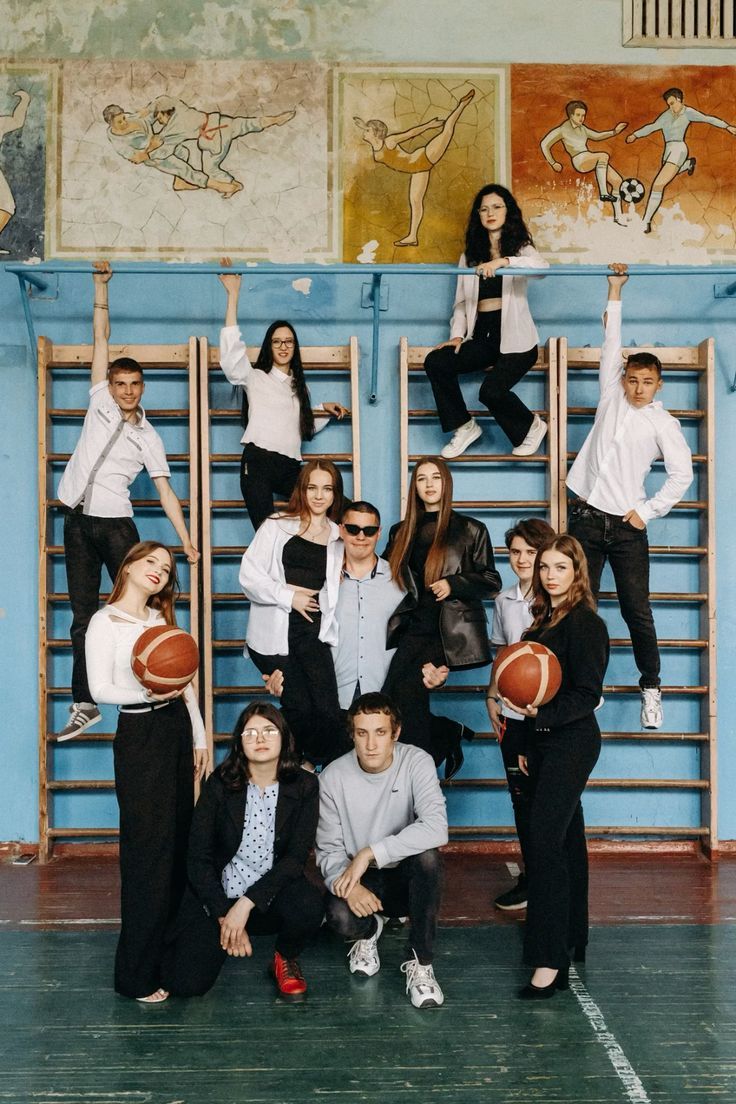 Group of students and teacher posing in a school gymnasium with basketball and wall murals.