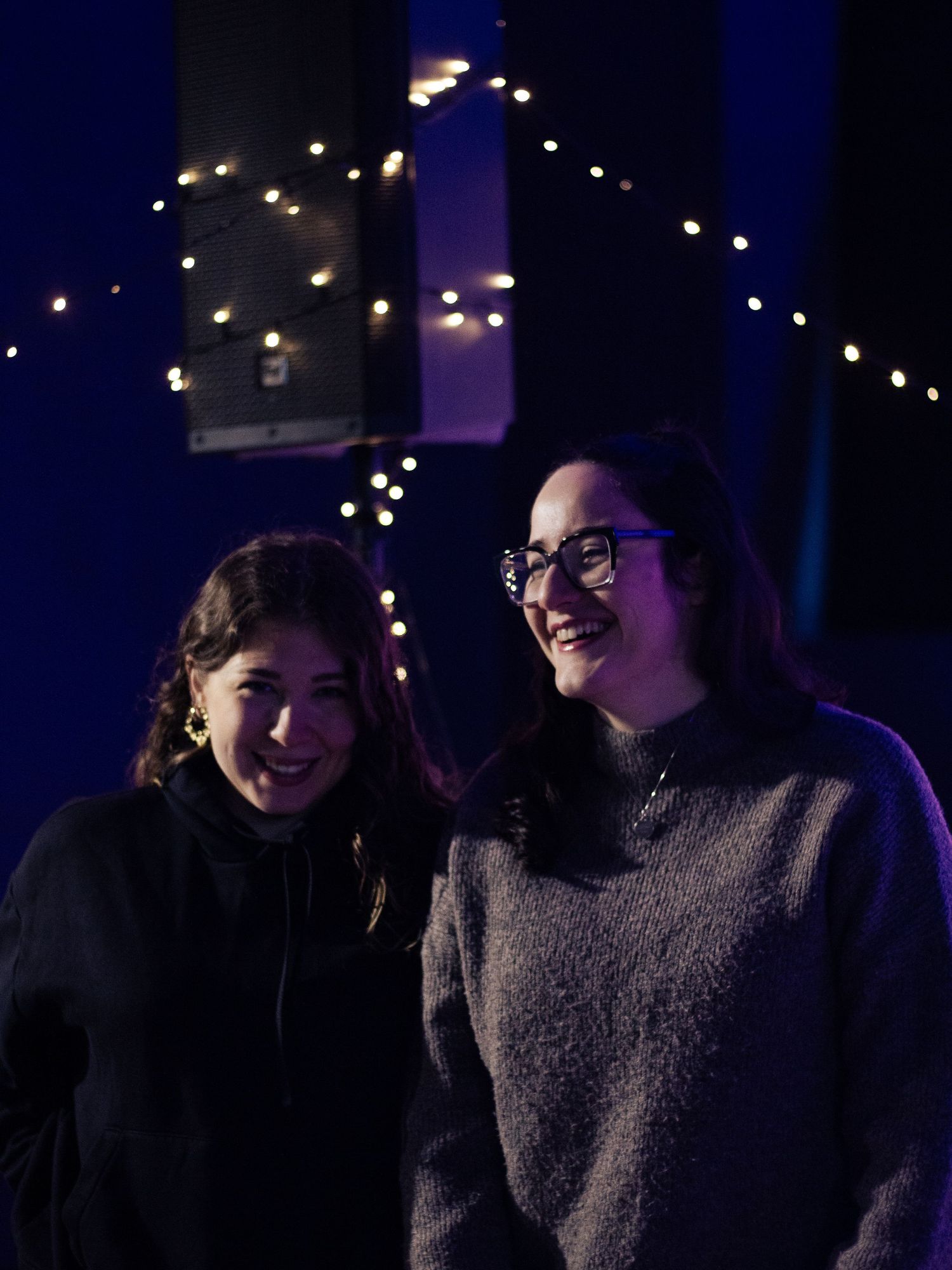 Two young ladies smiling with pixie lights in the backgorund.