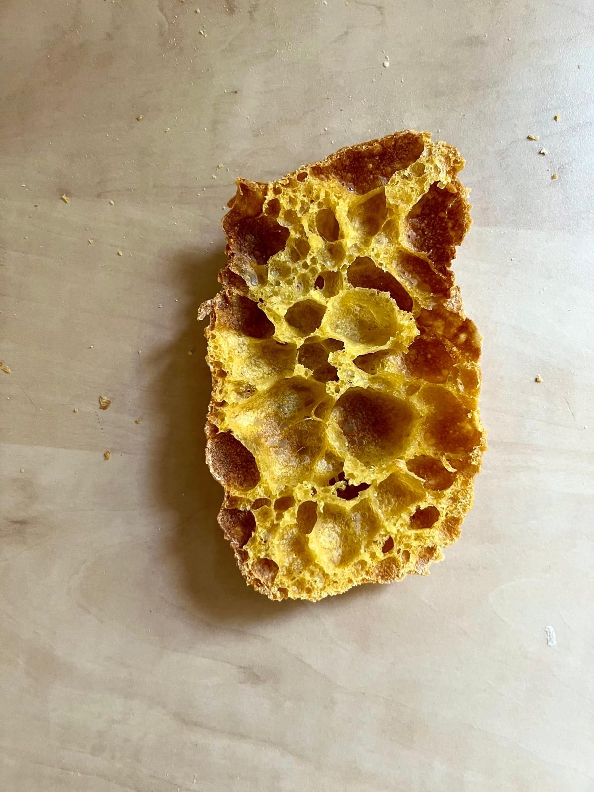 Single slice of golden turmeric sourdough bread with open airy crumb structure on wooden surface.