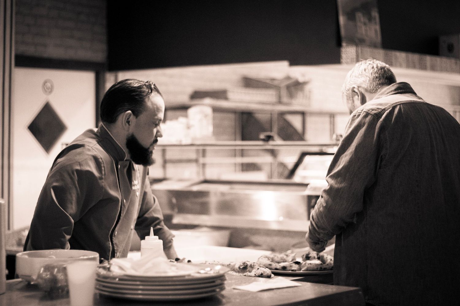 Two chefs working together at a kitchen counter in a dimly lit restaurant.
