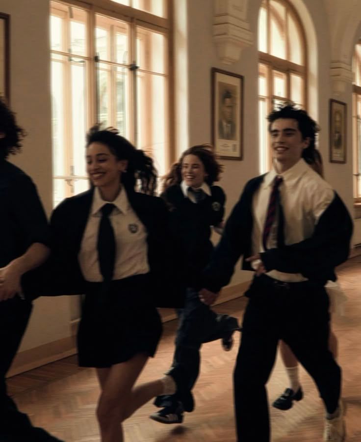 Students in school uniforms laughing and running through a bright hallway with large windows.