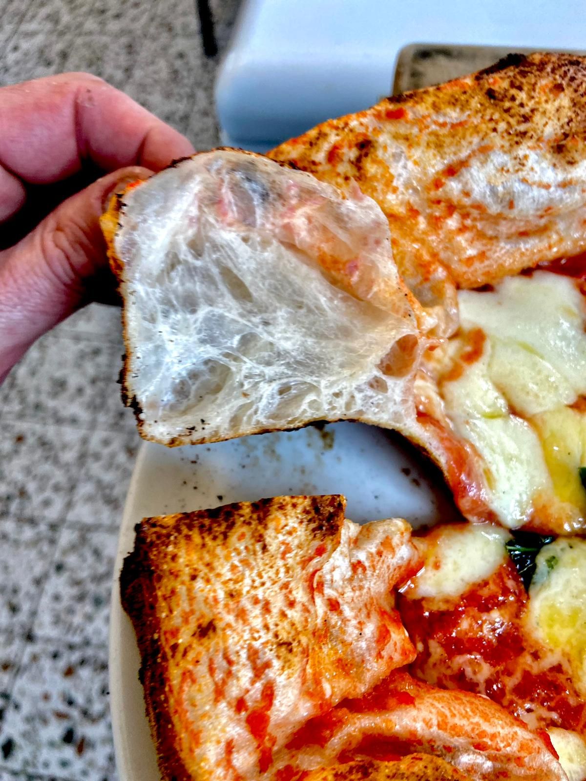 Hand lifting pizza slice showing light airy crust with tomato and cheese toppings.