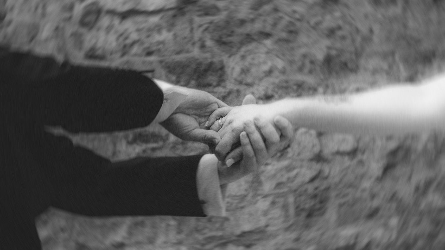 Black and white photo of a couple holding hands gently, showcasing a wedding ring, symbolizing love and commitment.