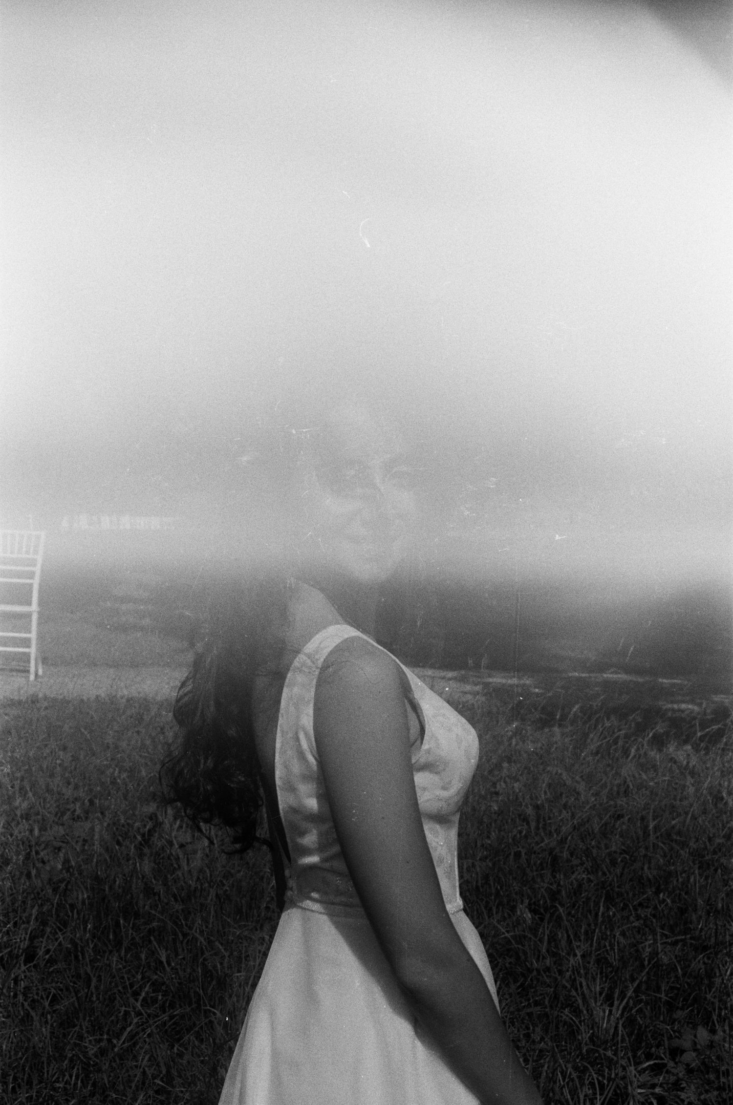 Dreamy overexposed black and white film photo of bride in white dress outdoors.