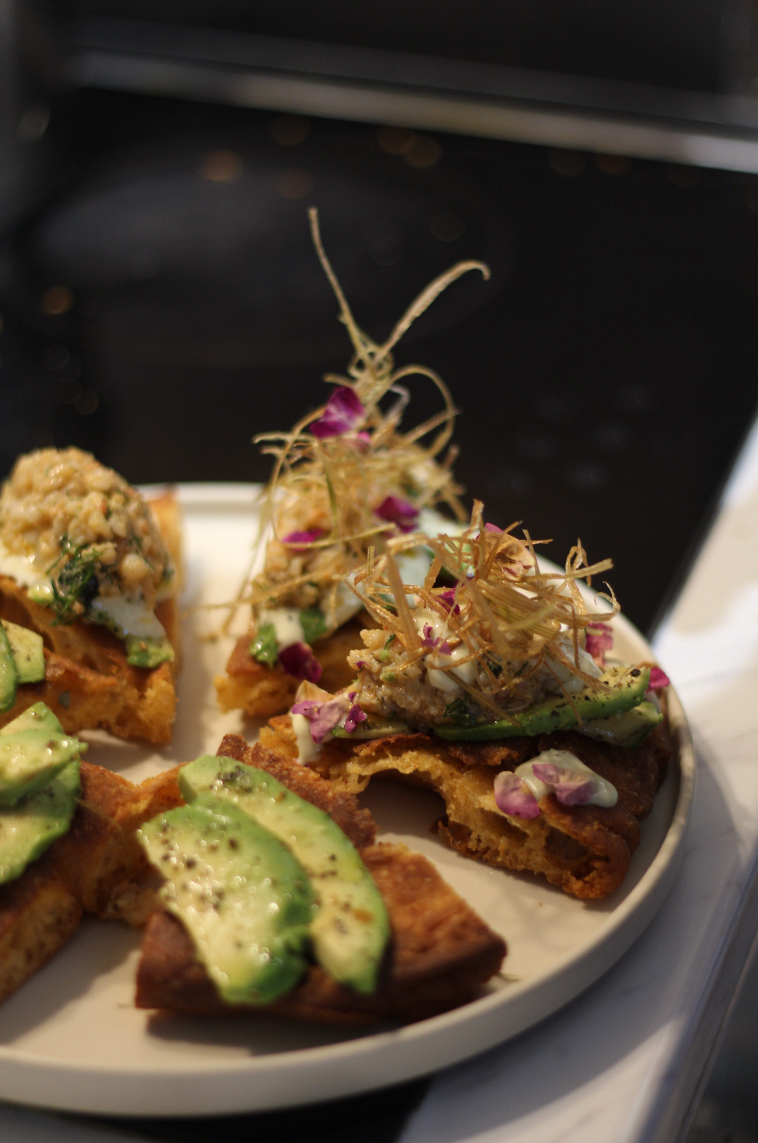 Gourmet pizza slices topped with avocado, microgreens, edible flowers, and crispy straw garnish on plate.