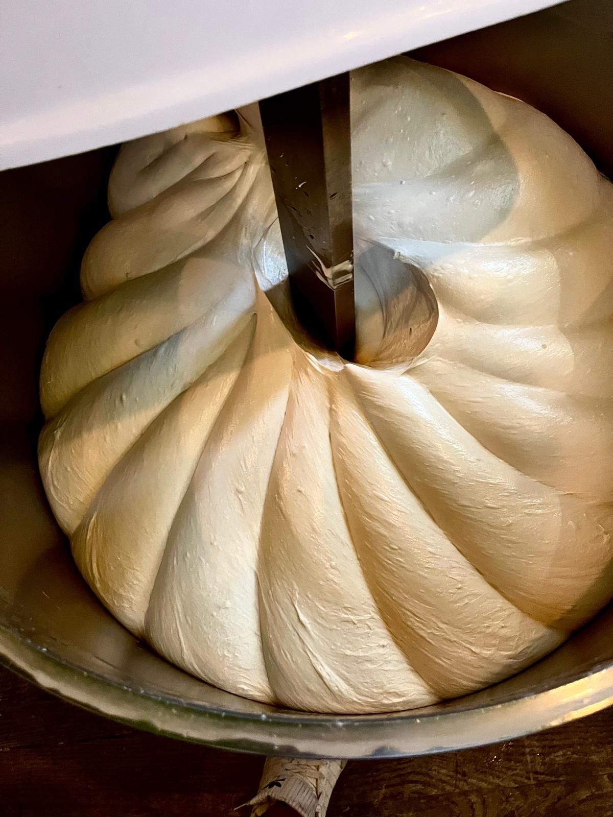 Smooth bread dough being kneaded by a spiral hook attachment in a commercial stand mixer bowl.