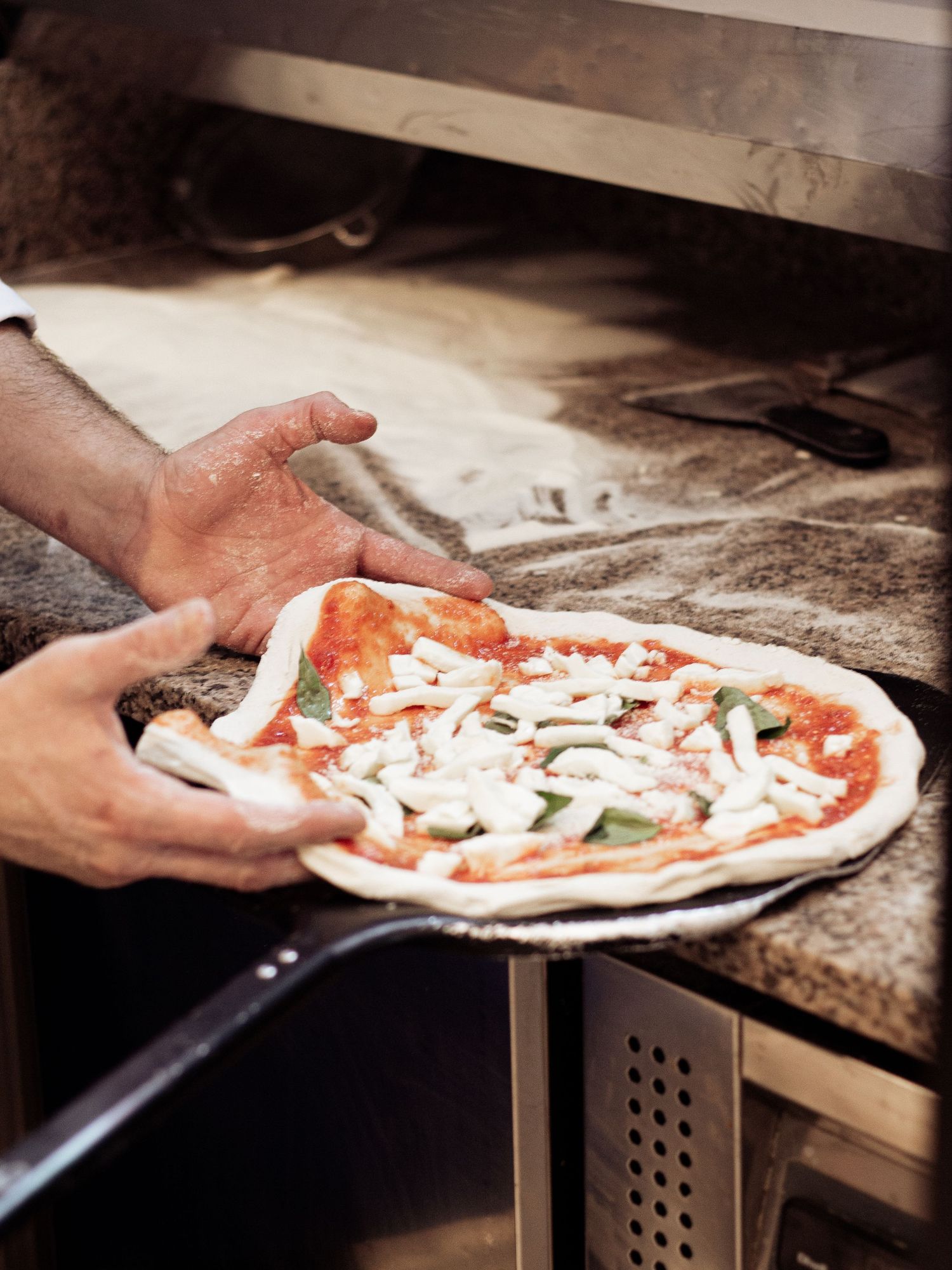 Chef sliding a topped Neapolitan pizza onto a peel before placing it in the oven.