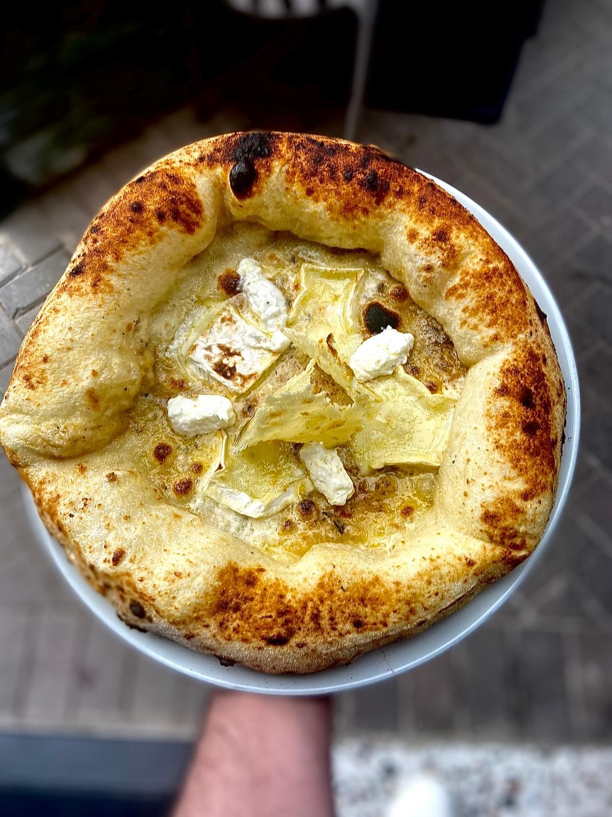 Neapolitan pizza with artichokes and goat cheese held up showing charred crust.