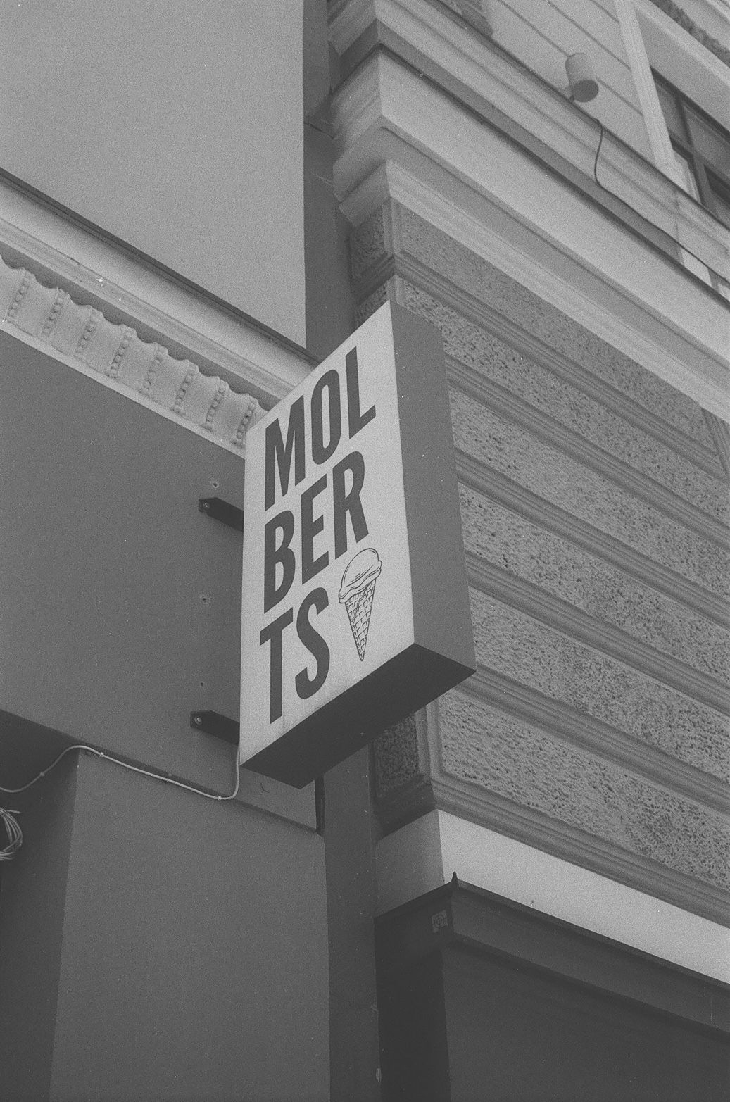 Black and white photo of Molberts ice cream shop sign with cone graphic mounted on building corner.