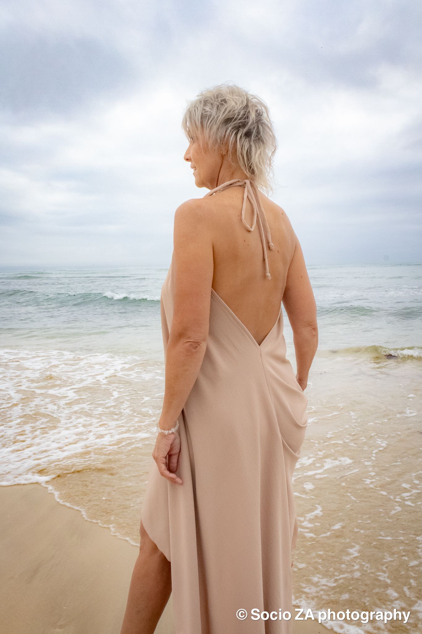 Woman standing in the water on the beach, wearing a low-back dress.