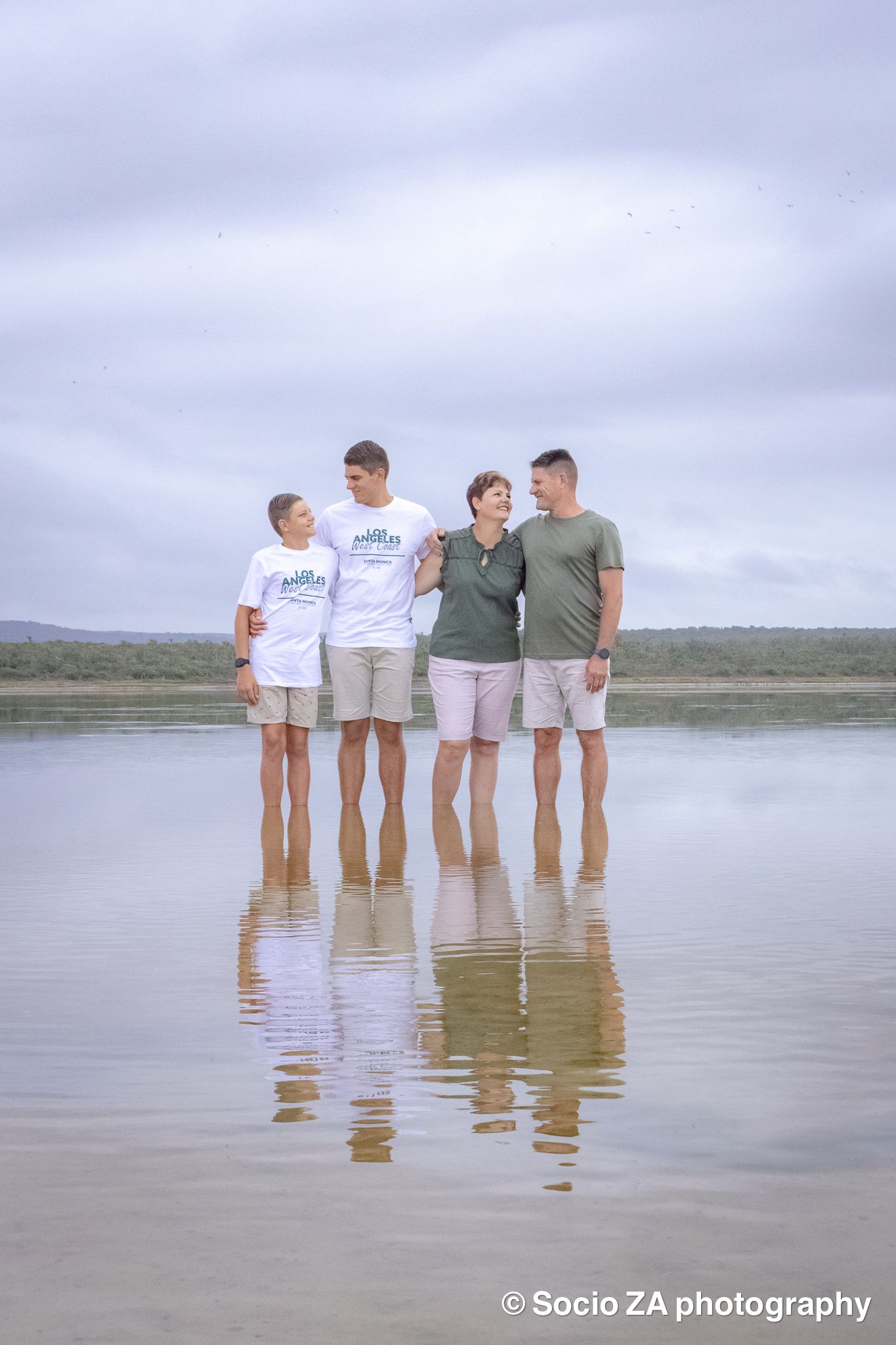 Family beach photoshoot in Jeffrey's Bay — beautiful backlit moment of family holding hands facing the ocean, by Socio ZA Photography, Easte