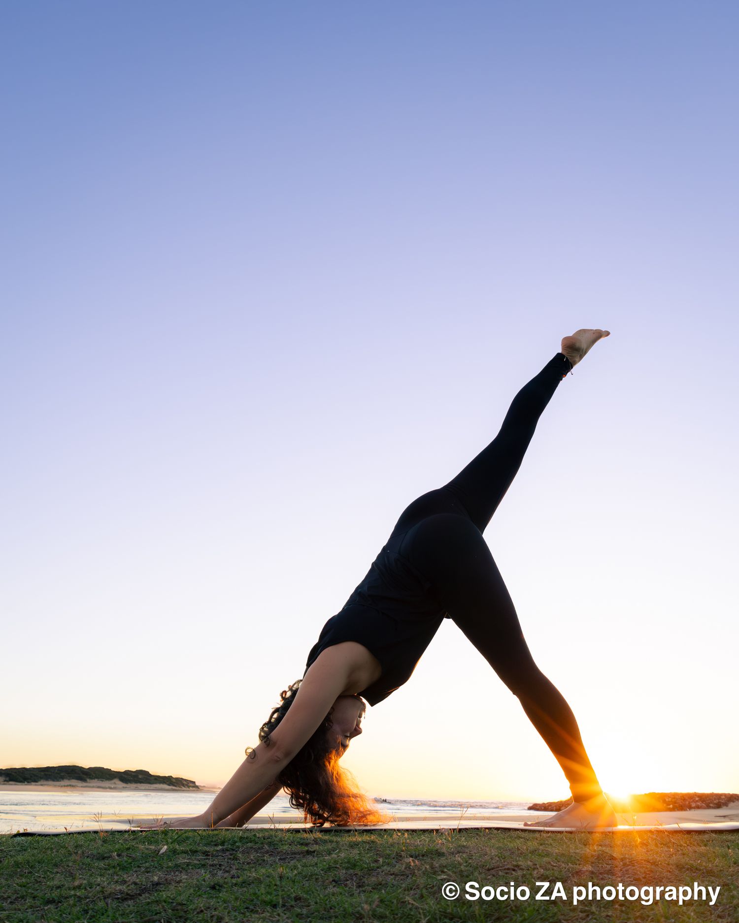 A woman doing a yoga pose at sunrise at the beach with the water and sun behind her. Eastern Cape St Francis Bay