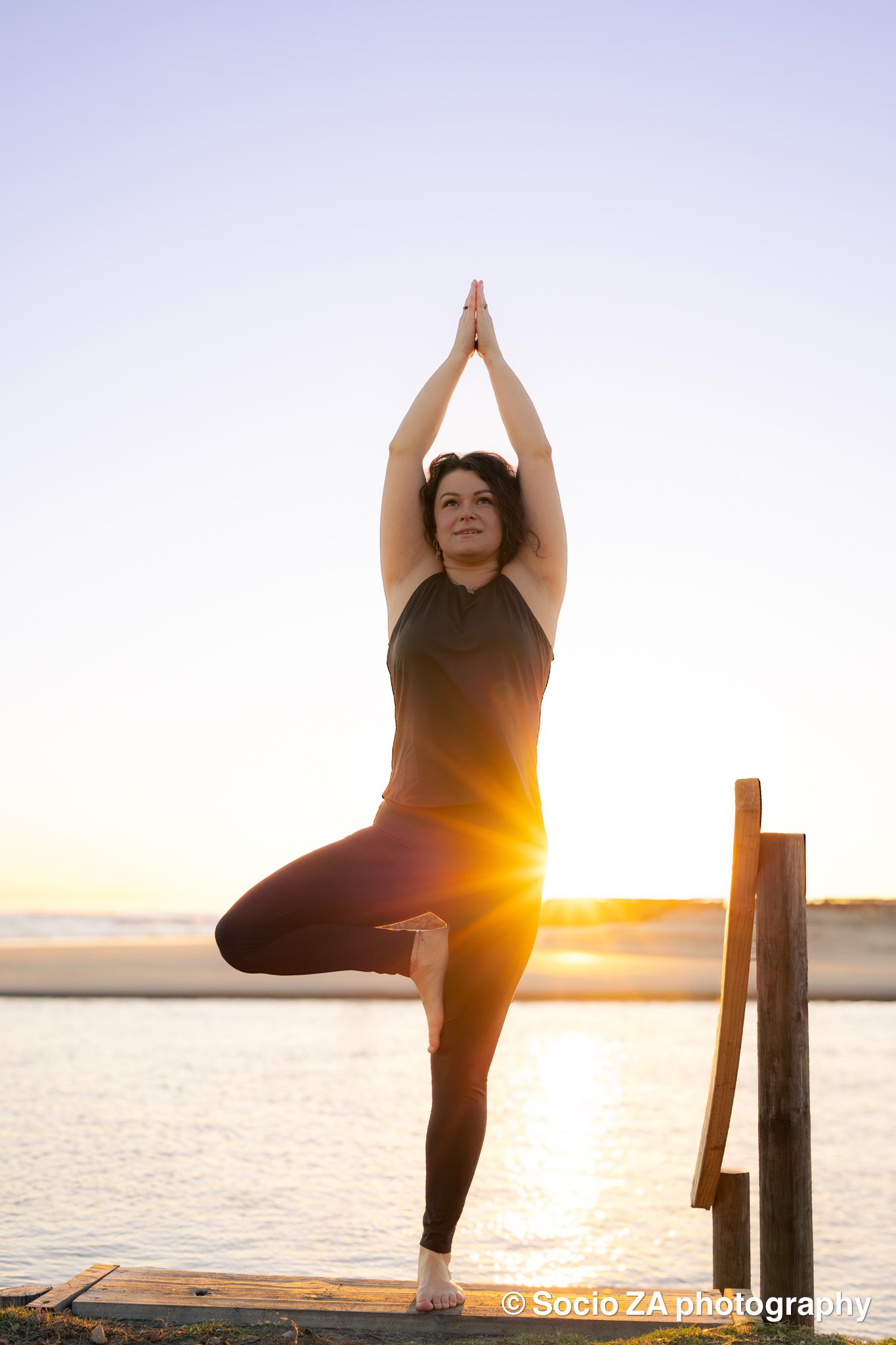 A woman doing a yoga pose at sunrise at the beach with the water and sun behind her. Eastern Cape St Francis Bay