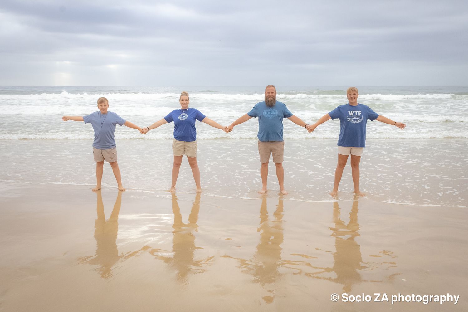 Family beach photoshoot in Jeffrey's Bay — beautiful backlit moment of family holding hands facing the ocean, by Socio ZA Photography