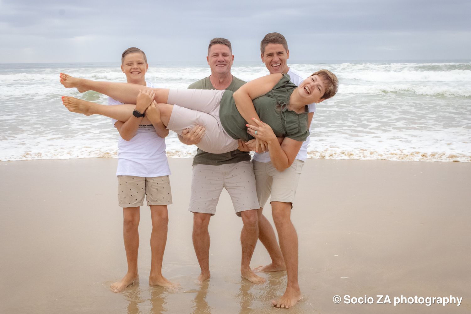 Family beach photoshoot in Jeffrey's Bay — beautiful backlit moment of family holding hands facing the ocean, by Socio ZA Photography.