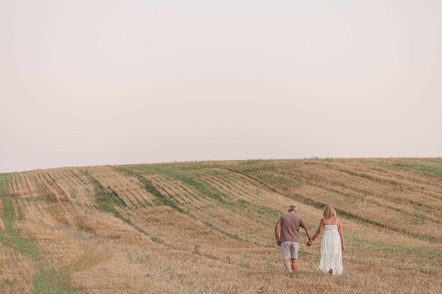 Couple walking through harvested farm field at sunset.