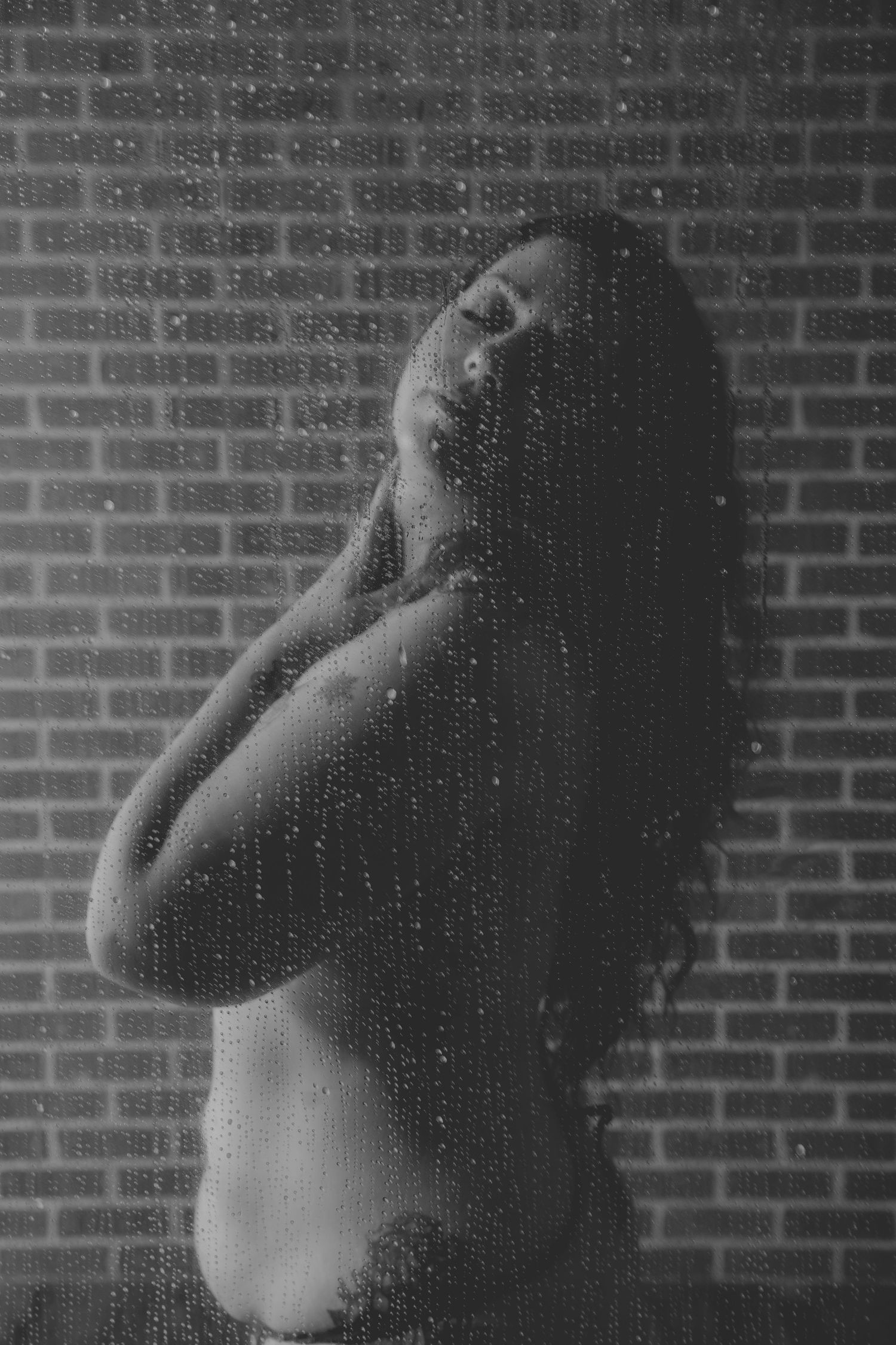 Moody black and white portrait with raindrops on glass creating a dreamy effect.