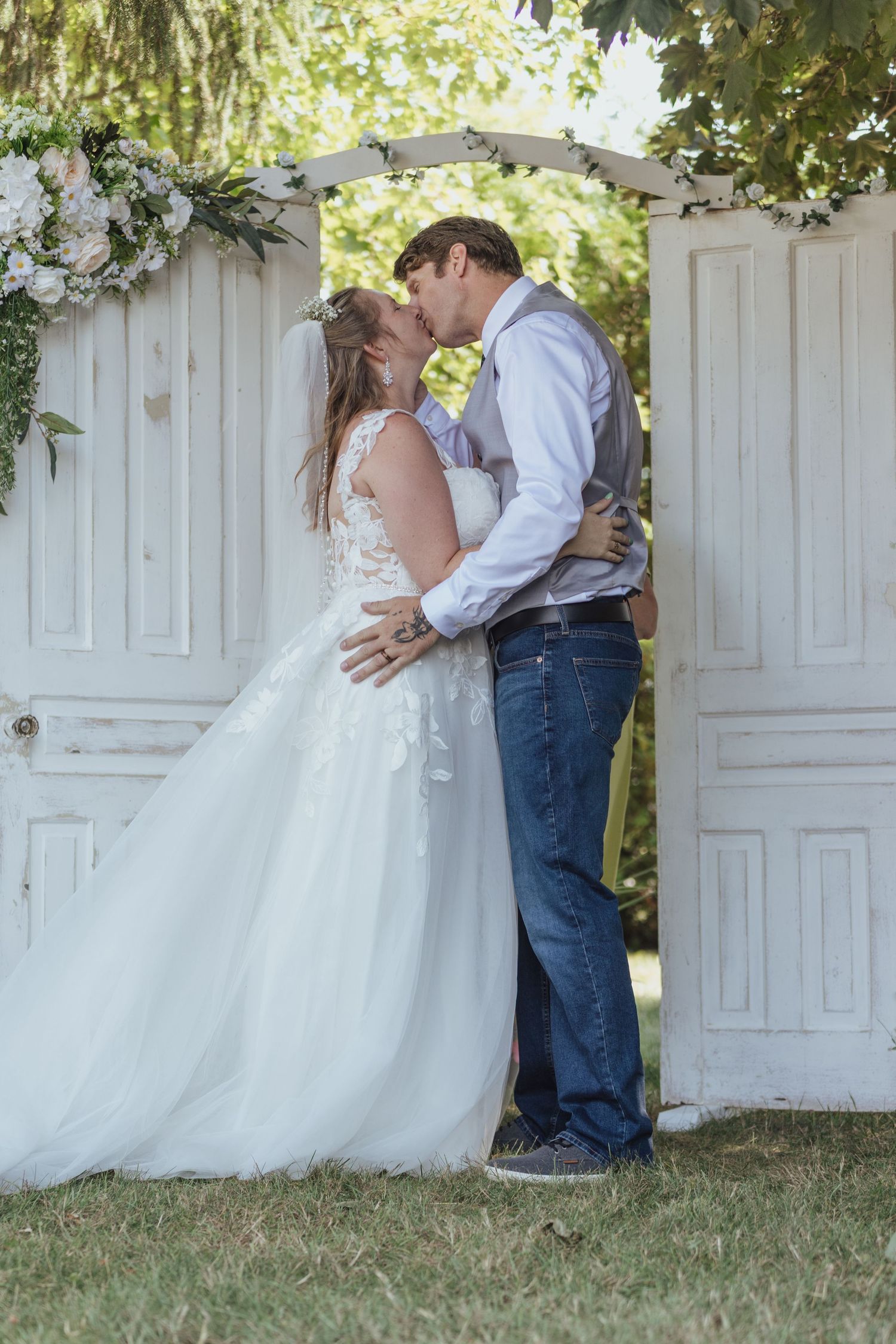 Wedding couple shares intimate moments against white vintage door backdrop with floral decorations.