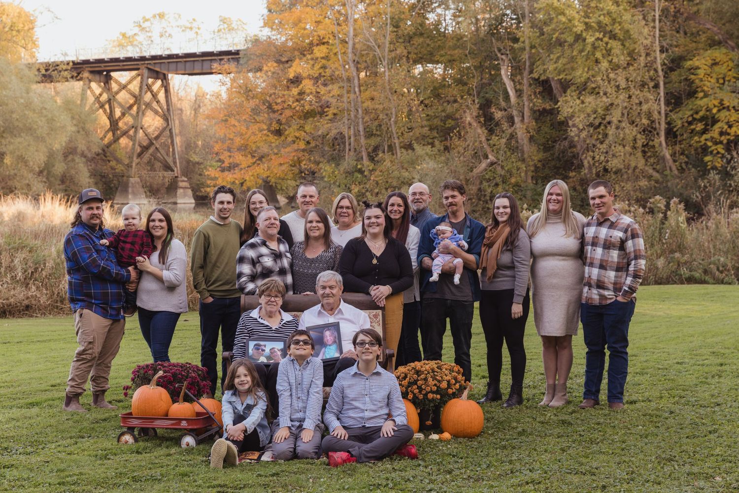 Extended family gathering outdoors with pumpkins and fall foliage in the background.