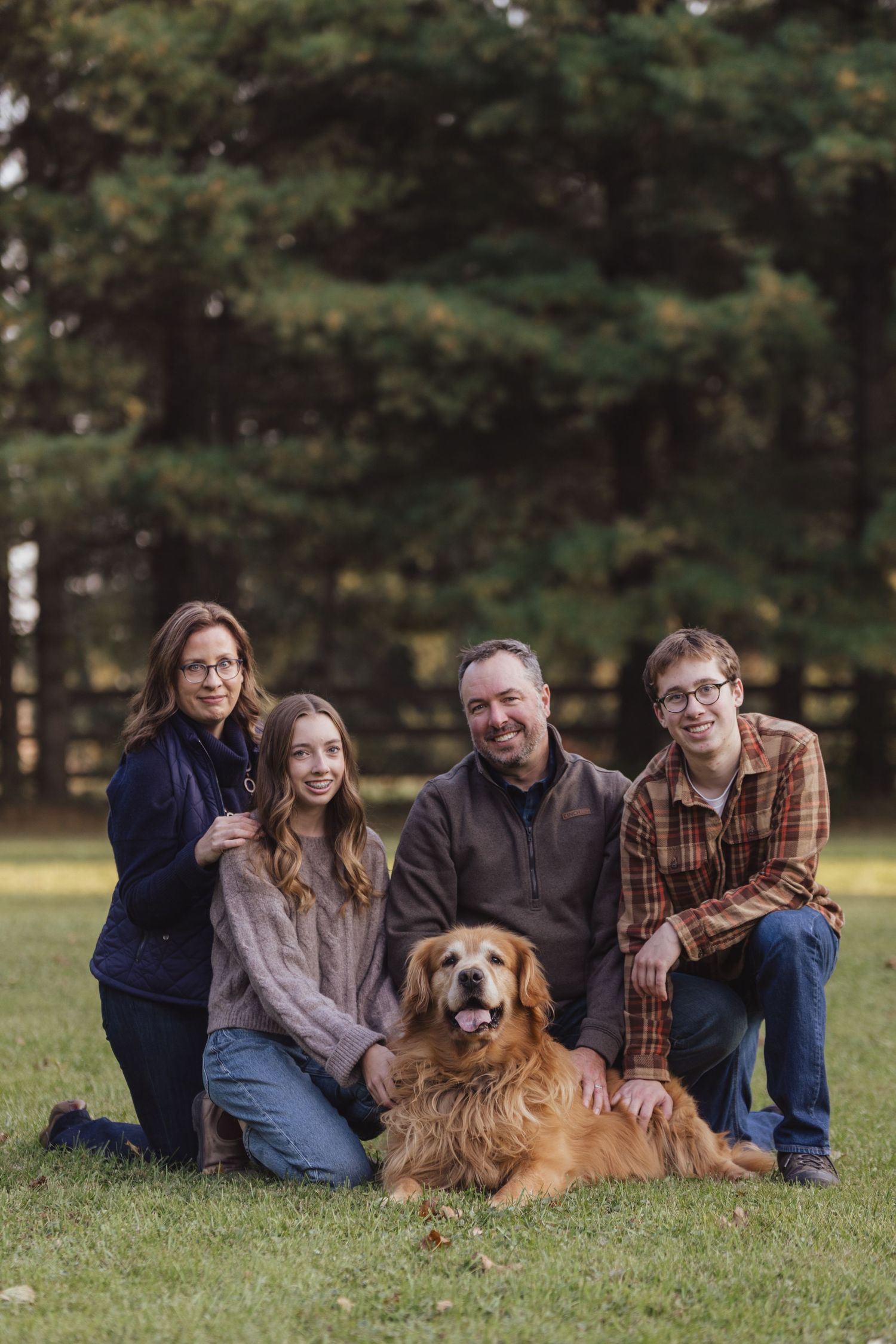 Family relaxing on grass with their golden retriever during an outdoor photo session.