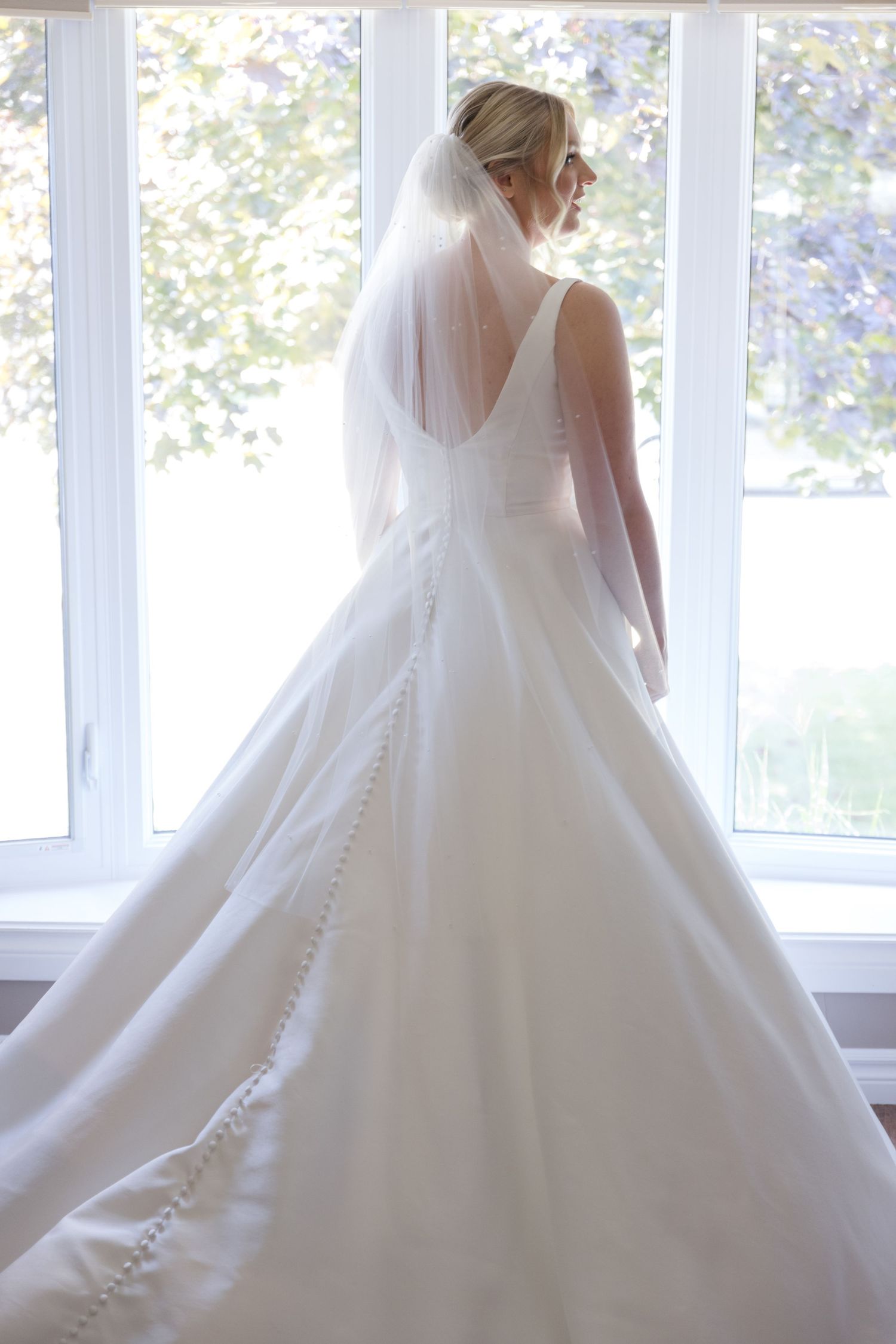 Elegant white wedding dress with flowing skirt photographed near bright windows.