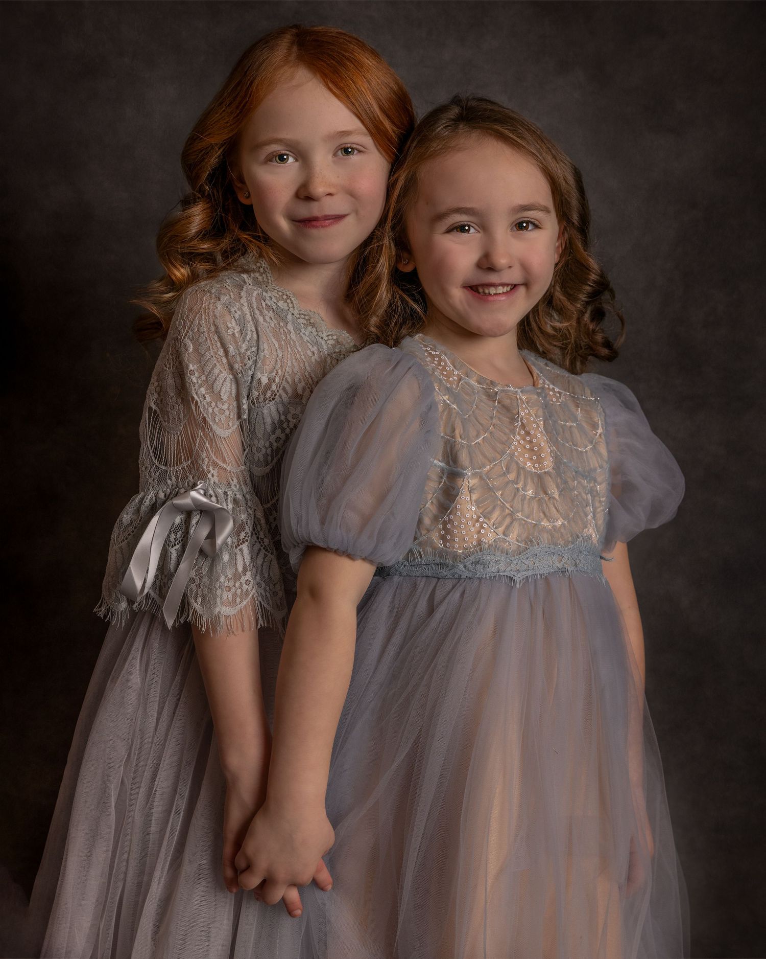 Two children in elegant lace dresses pose together for a formal portrait.