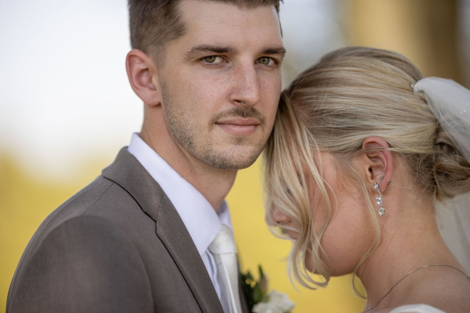 Romantic wedding couple embraces in a sunlit outdoor setting.
