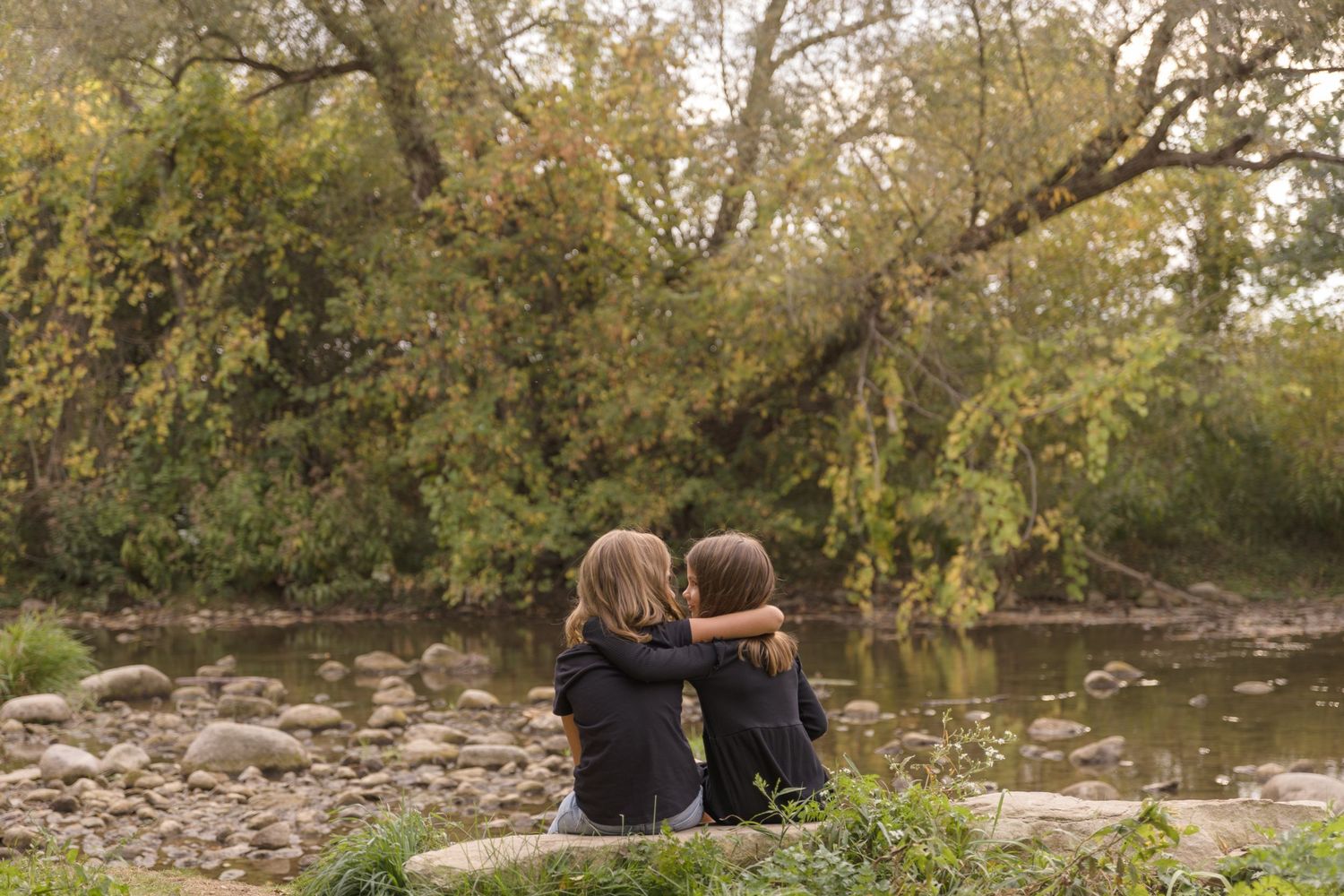 People sitting together on rocks by a peaceful riverside at sunset.