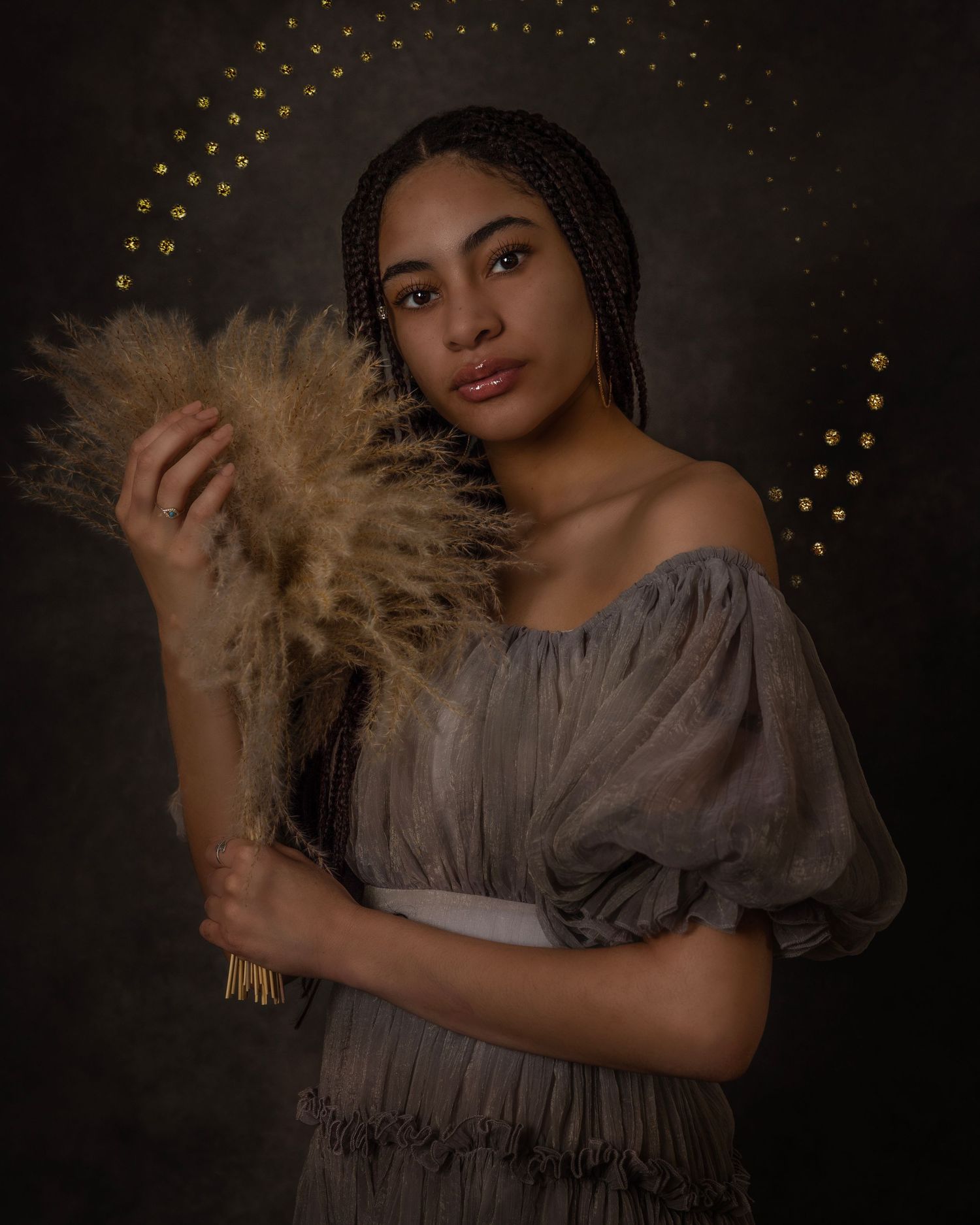 Artistic portrait with golden sparkles and flowing gray dress against dark background.