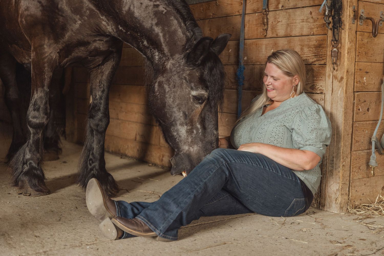 Horse and person resting together in a rustic wooden stable.