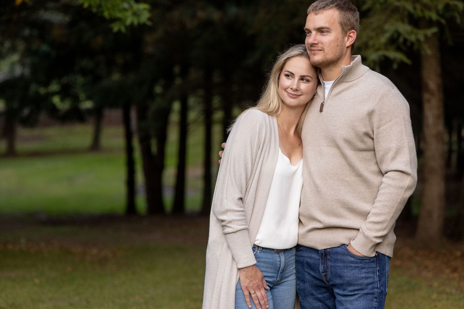Casual couple in neutral tones embracing outdoors in a park setting.
