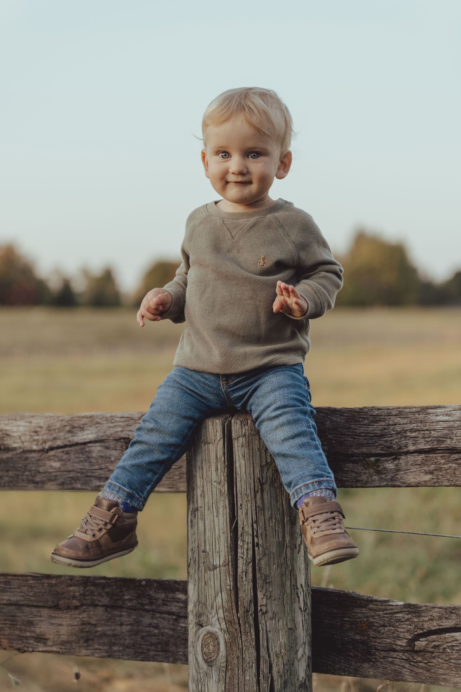 Little one sitting on rustic wooden fence post in casual attire.