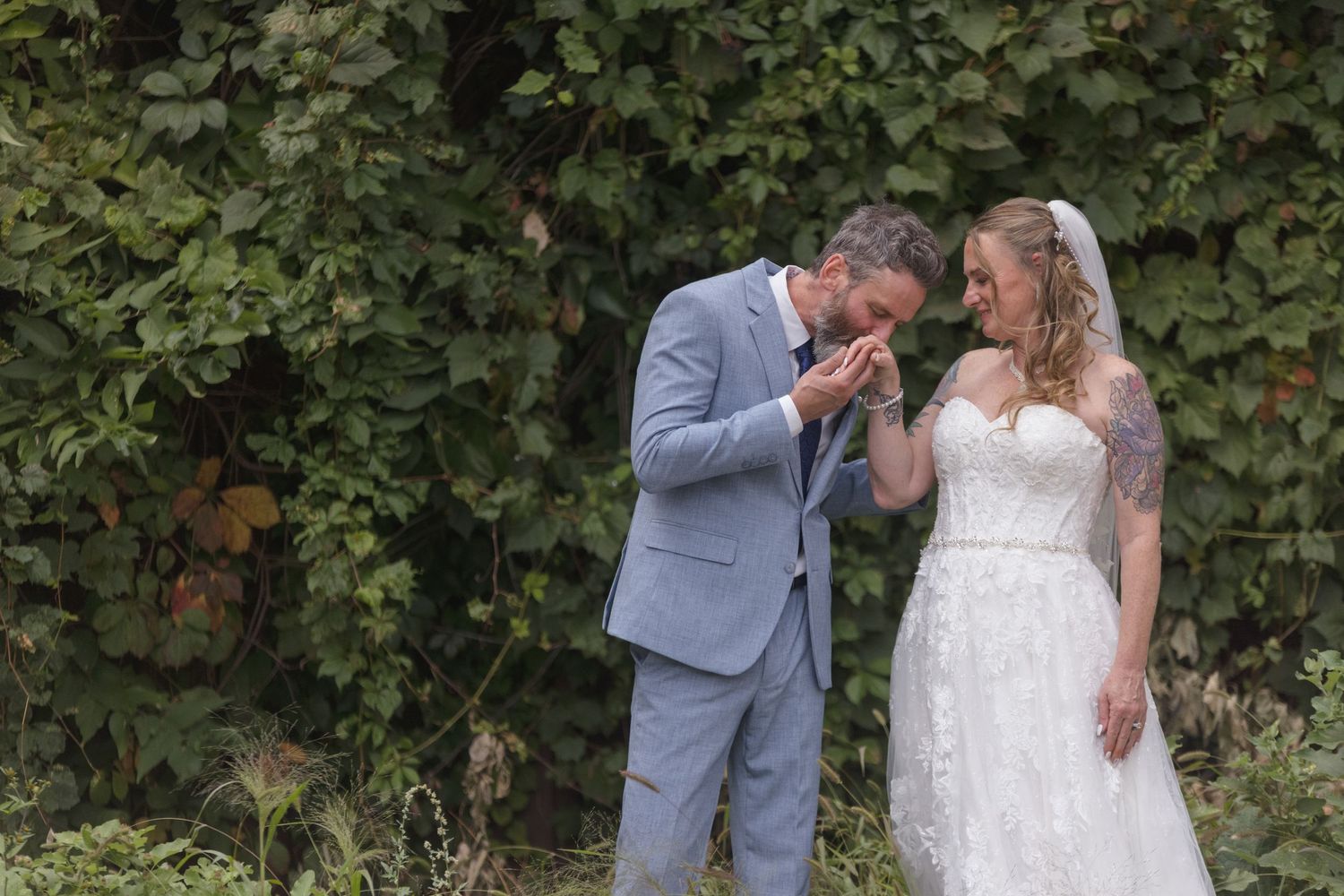 Couple in formal attire share tender moments against natural foliage backdrop.