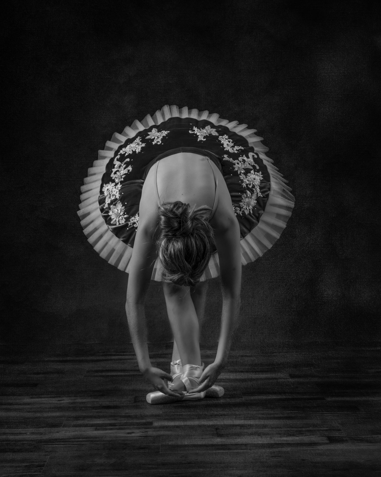 Black and white portrait of a ballet dancer bending forward in a tutu.