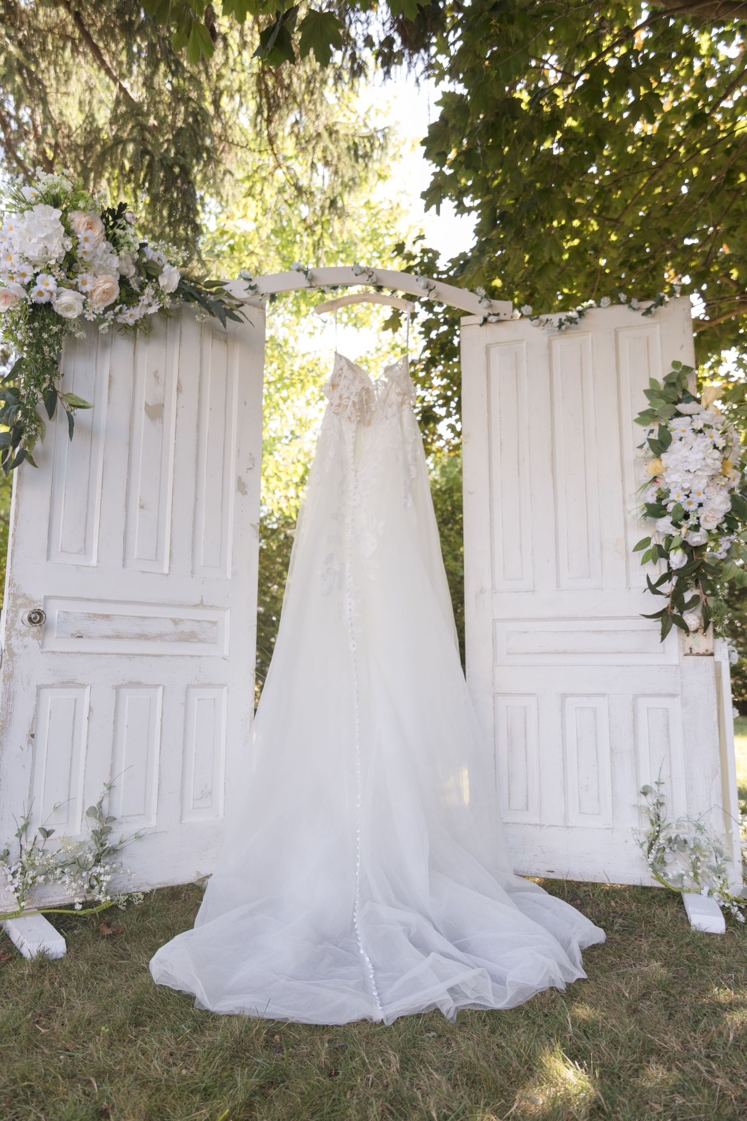 White vintage doors decorated with floral arrangements create elegant wedding backdrop outdoors.