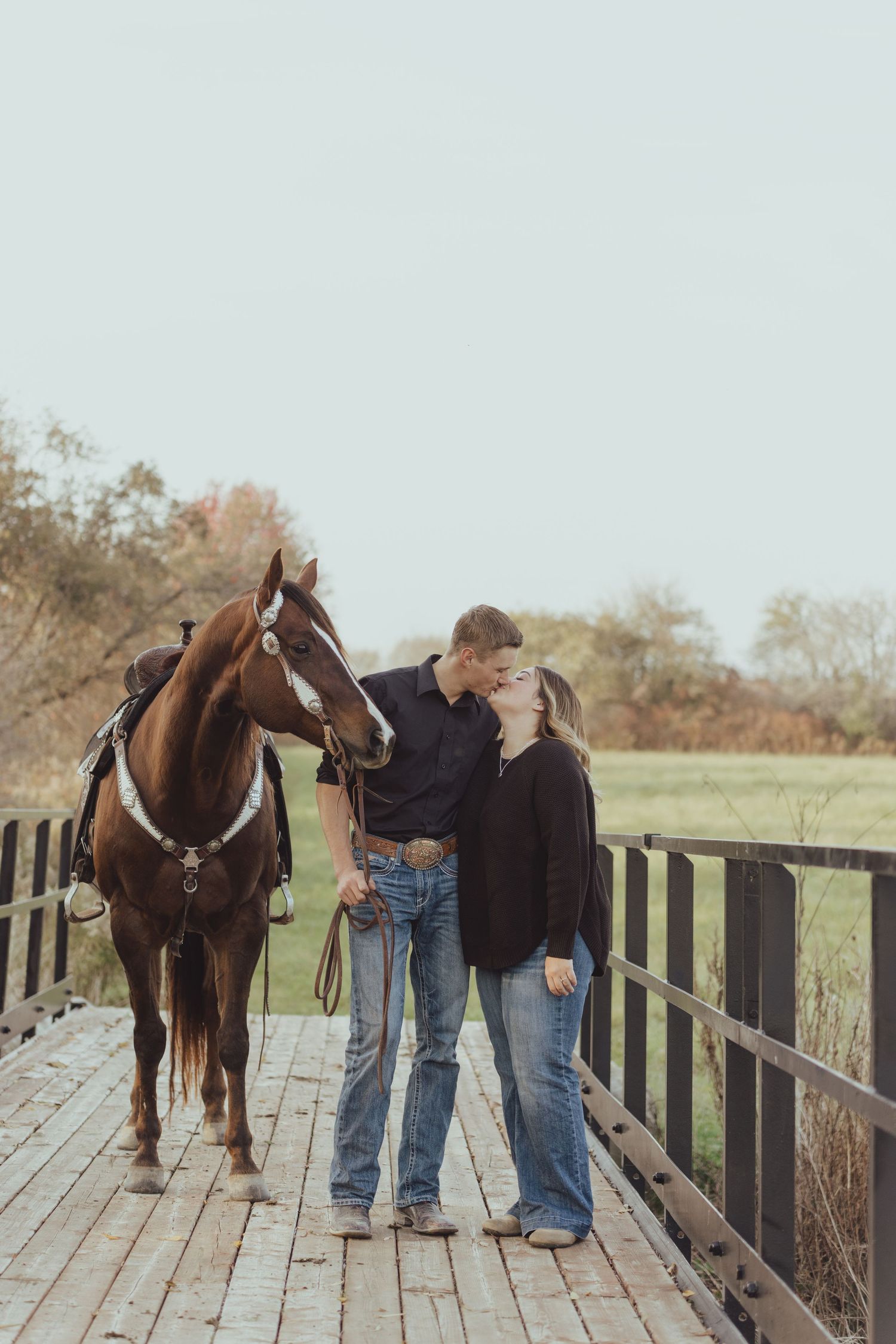 Horse and people standing together on a wooden bridge in a pastoral setting.