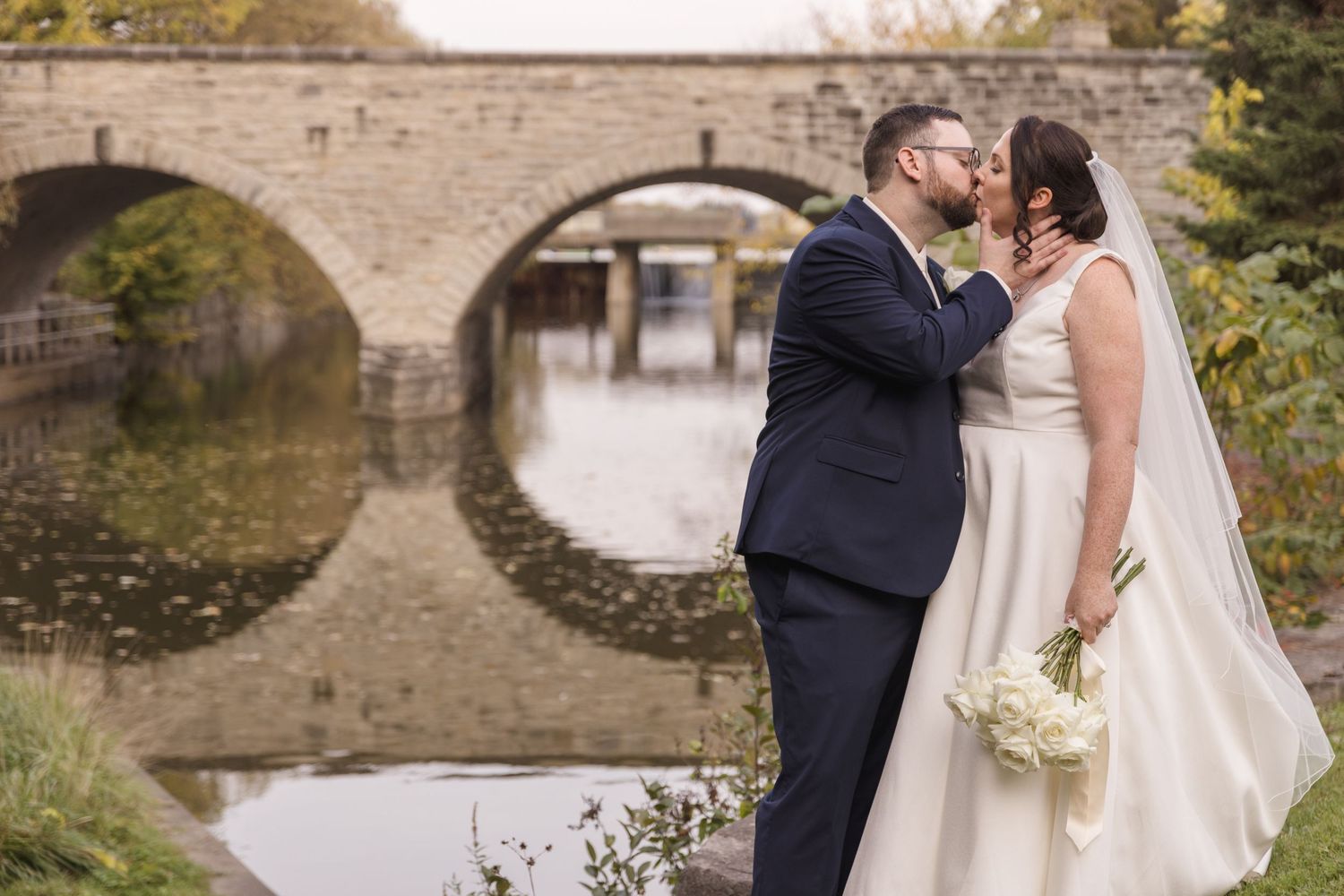 Wedding couple sharing an intimate moment by a stone bridge.