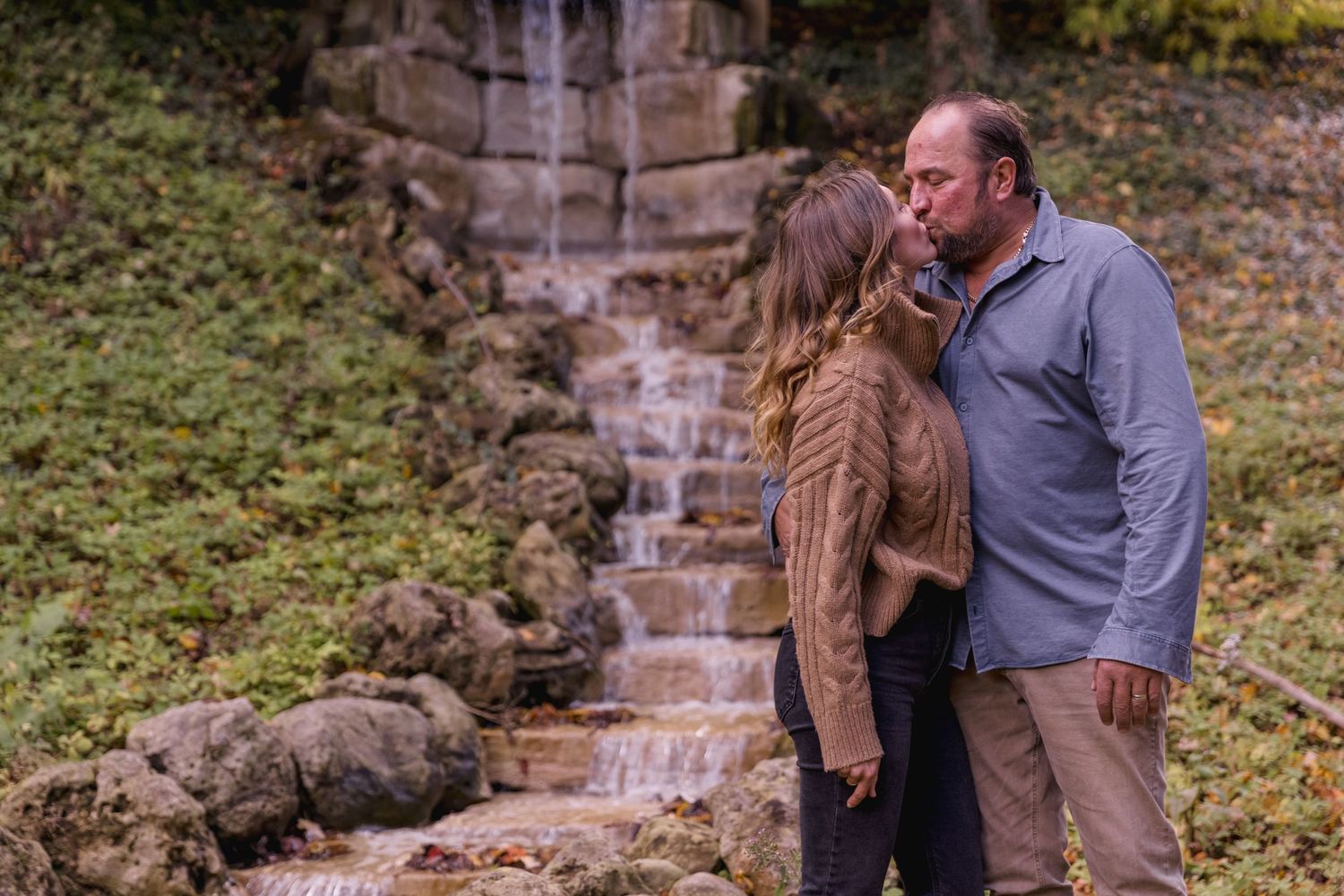People pose together by a scenic waterfall surrounded by fall foliage.