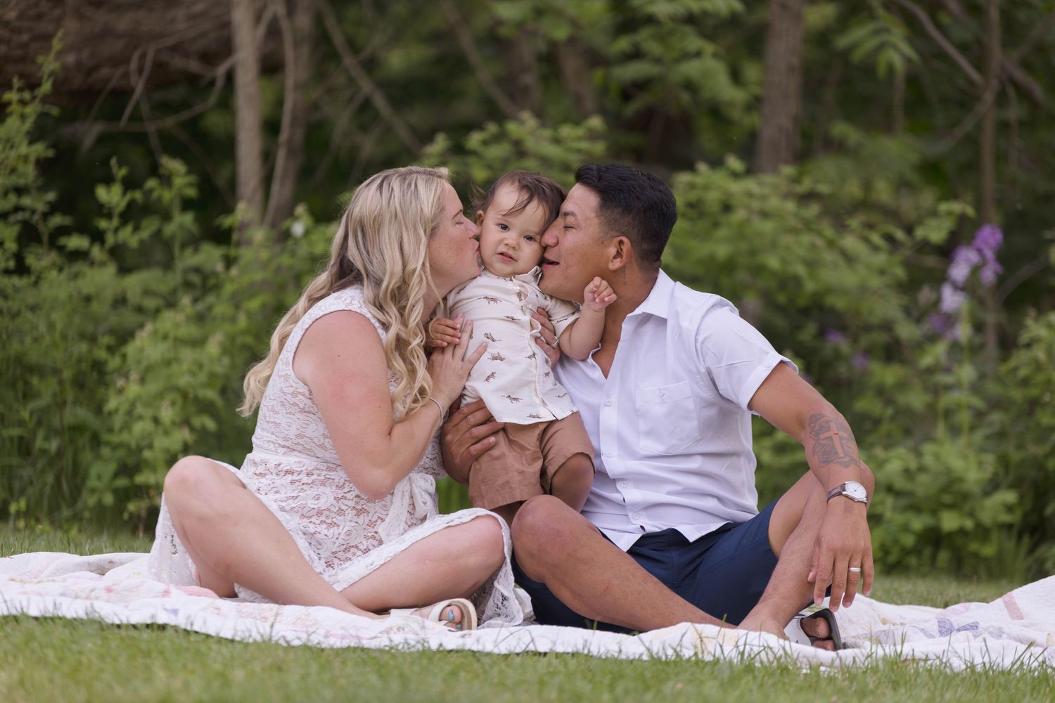 Intimate family moments captured on a white blanket in a lush green setting.