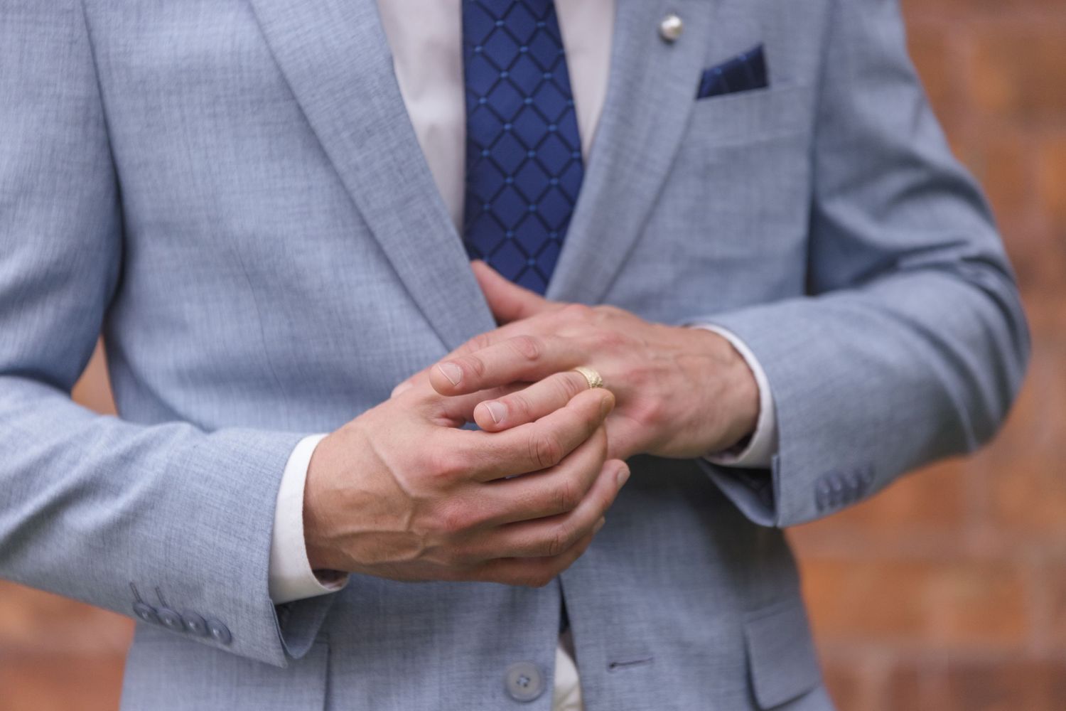 Close-up details of hands and formal attire in light blue wedding suit.