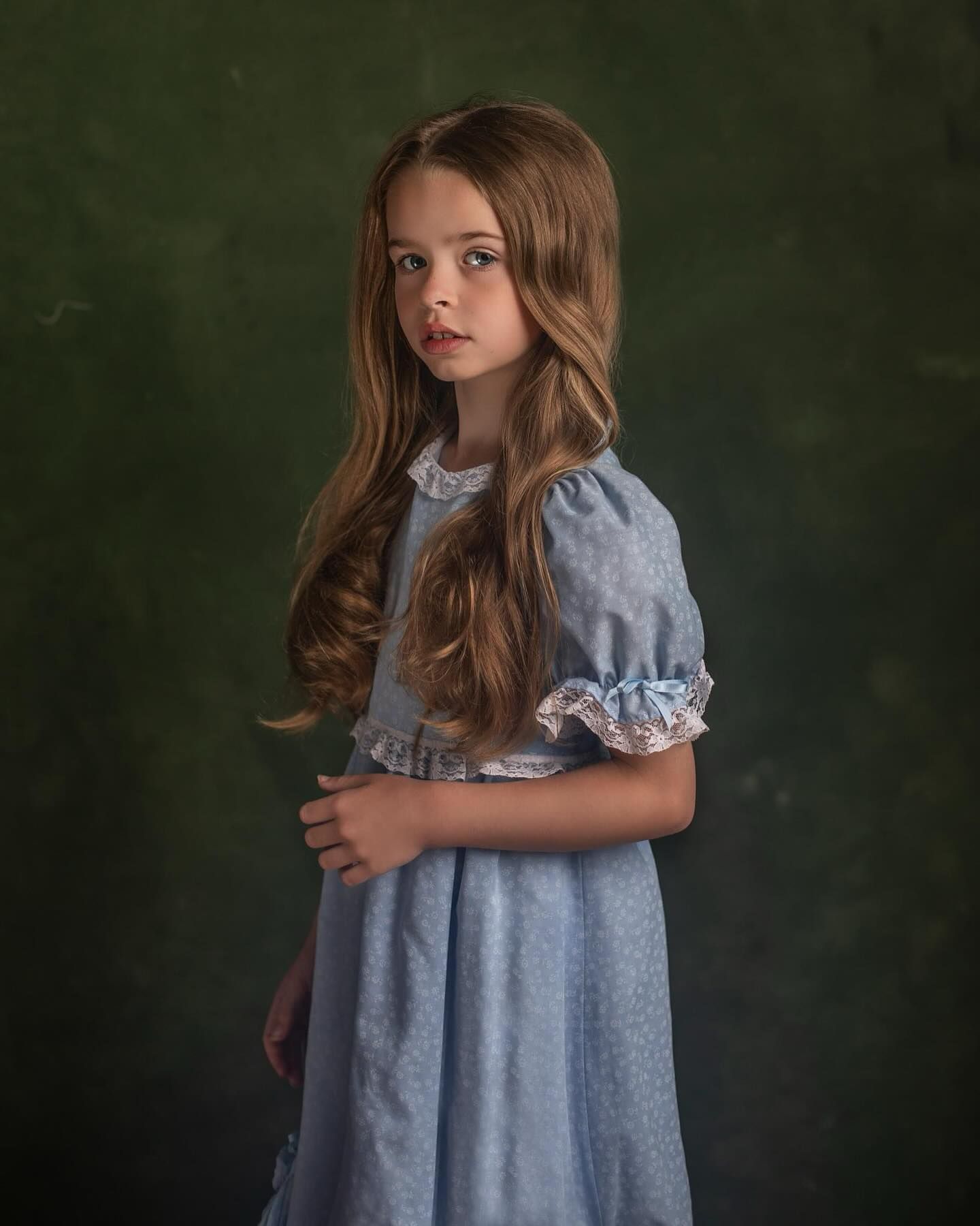 Child in a blue dress photographed in a series of dreamy poses against a dark green background.
