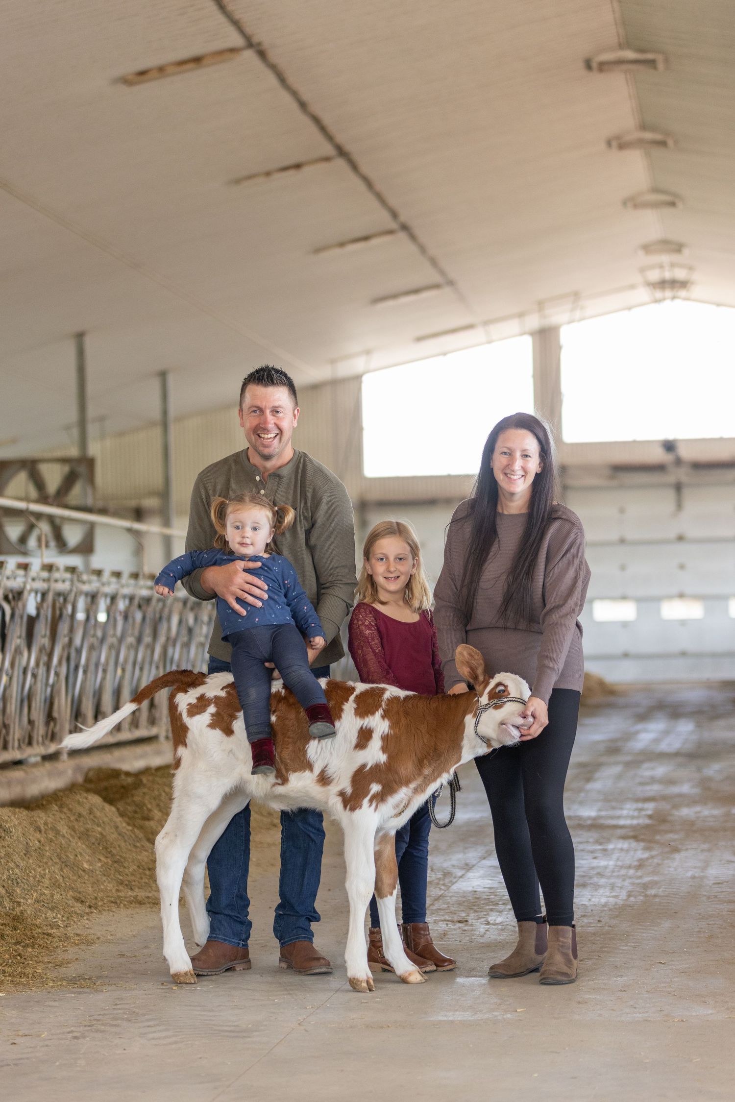 Family poses with young calf inside a rustic barn setting.