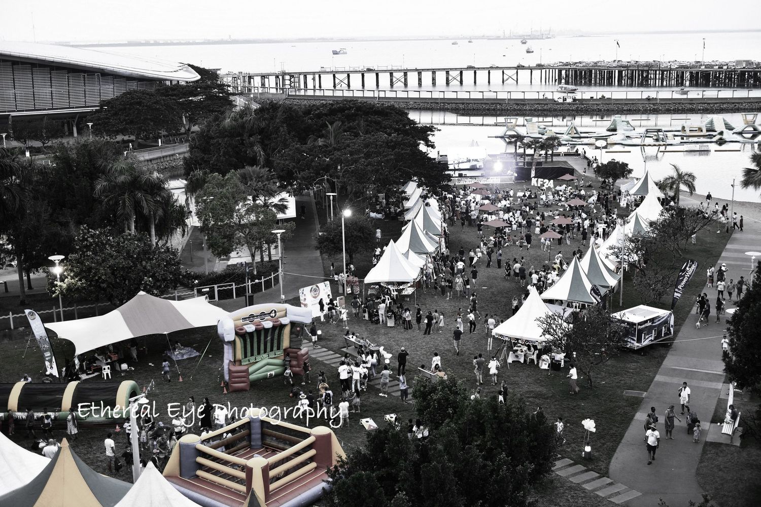 Black and white aerial view of an outdoor event with tents, crowds, and parked vehicles.