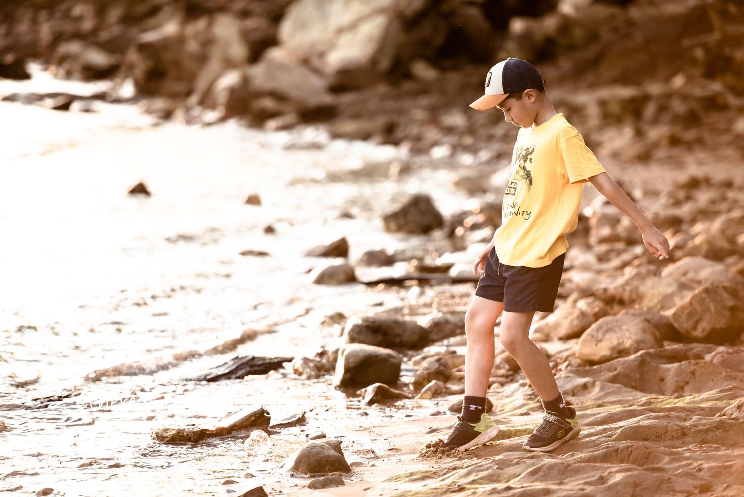Children walking along rocky shoreline during sunset with warm sepia tones.